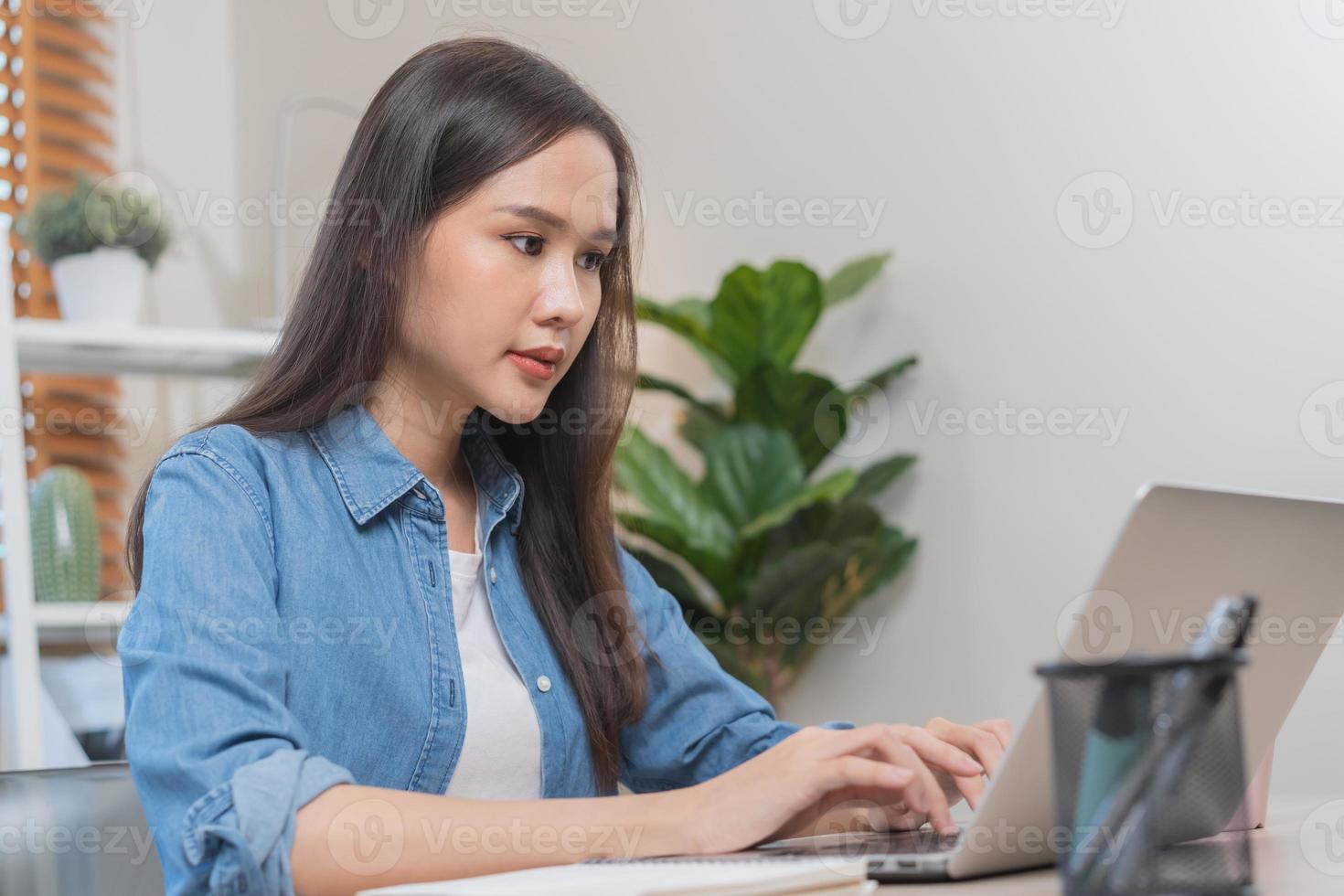 Beautiful asian young business woman looking on screen web, using laptop computer, sitting at home office, freelancer working. Technology, social distance. photo