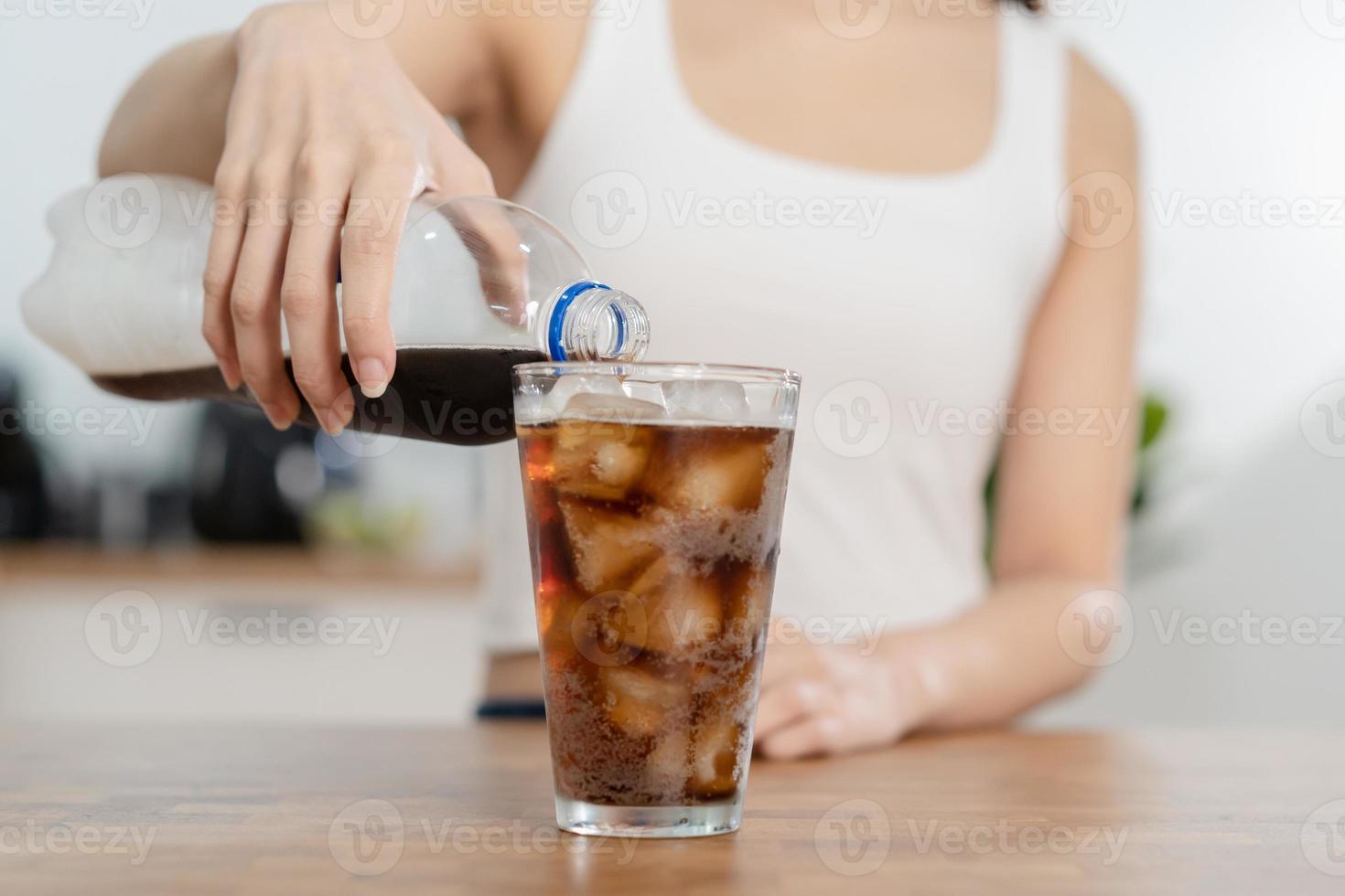 Thirsty, asian young woman, girl holding,  pouring cold cola soft drink soda, sparkling water with ice sweet sugar from bottle into glass in her hand. Health care, healthy diet lifestyle concept. photo