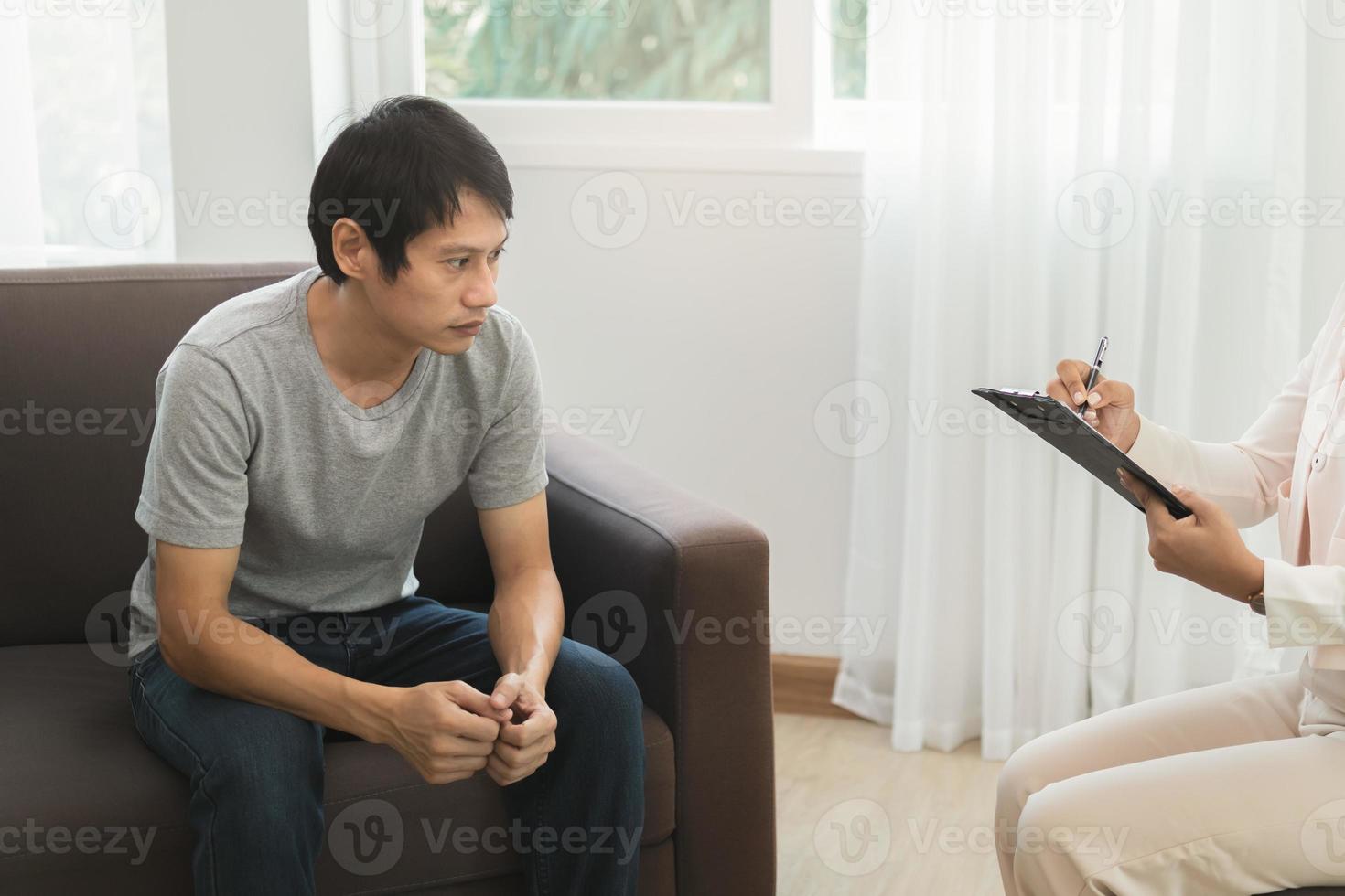 Sick,illness Asian young man mental symptom which must have been therapy, stress, sit on couch consult with psychologist, doctor woman take notes treat by therapist at clinic. Health care, sad person. photo