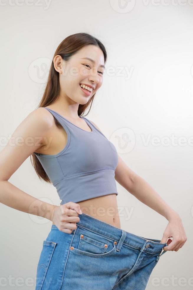 Shape slender, thin waist, attractive slim asian young woman, hand show shape her weight loss, wearing in big, large or oversize jeans, excess lose by diet and exercise. People body fit healthy. photo