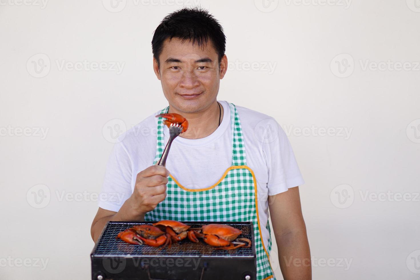 Asian man chef is cooking, grilling seafood on stove. Grilled craps. Concept, love cooking. Prepare meal for party or family. Kitchen lifestyle. Thai enjoy having seafood barbeque when they have party photo