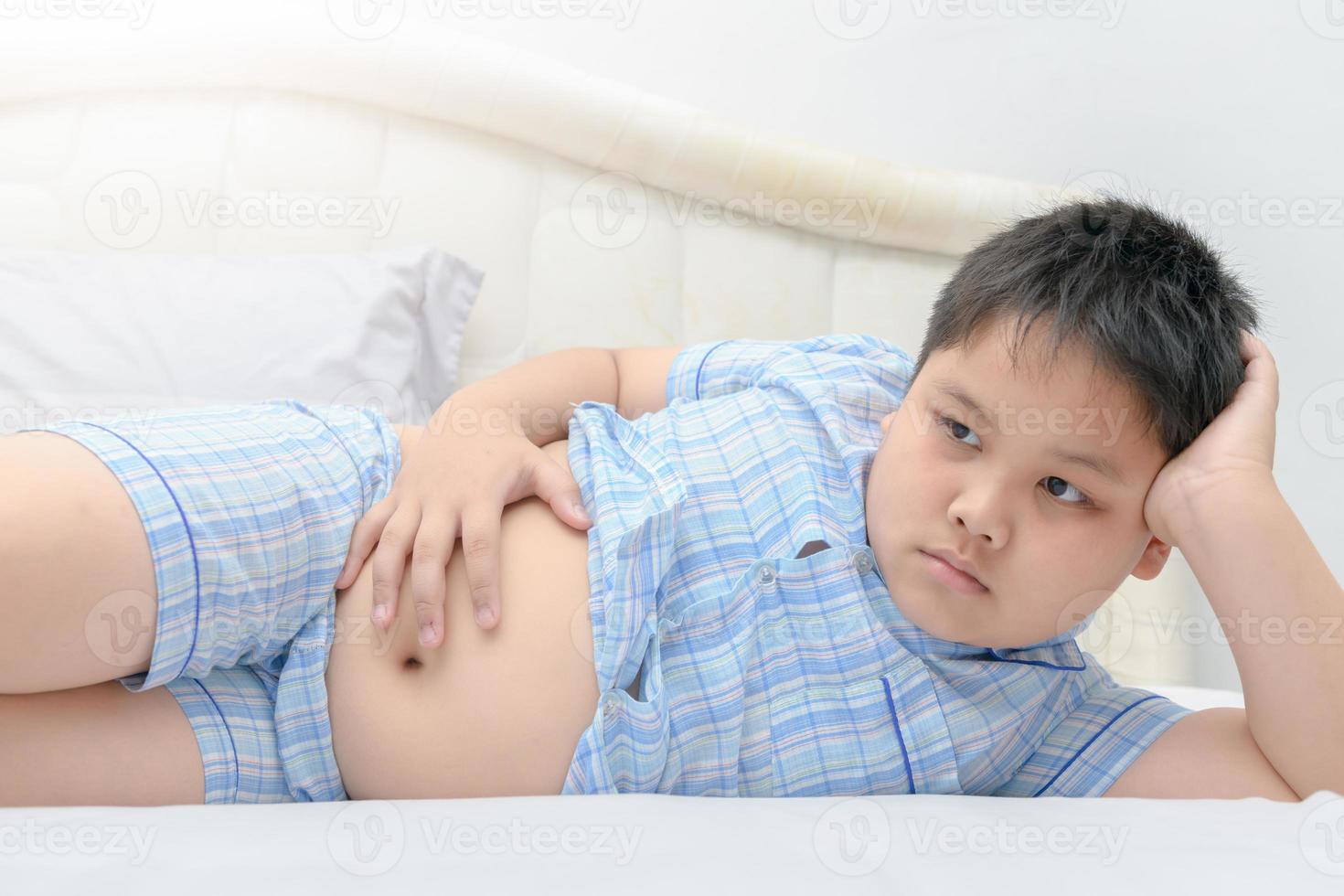 Obese fat boy lying show stomach on bed photo