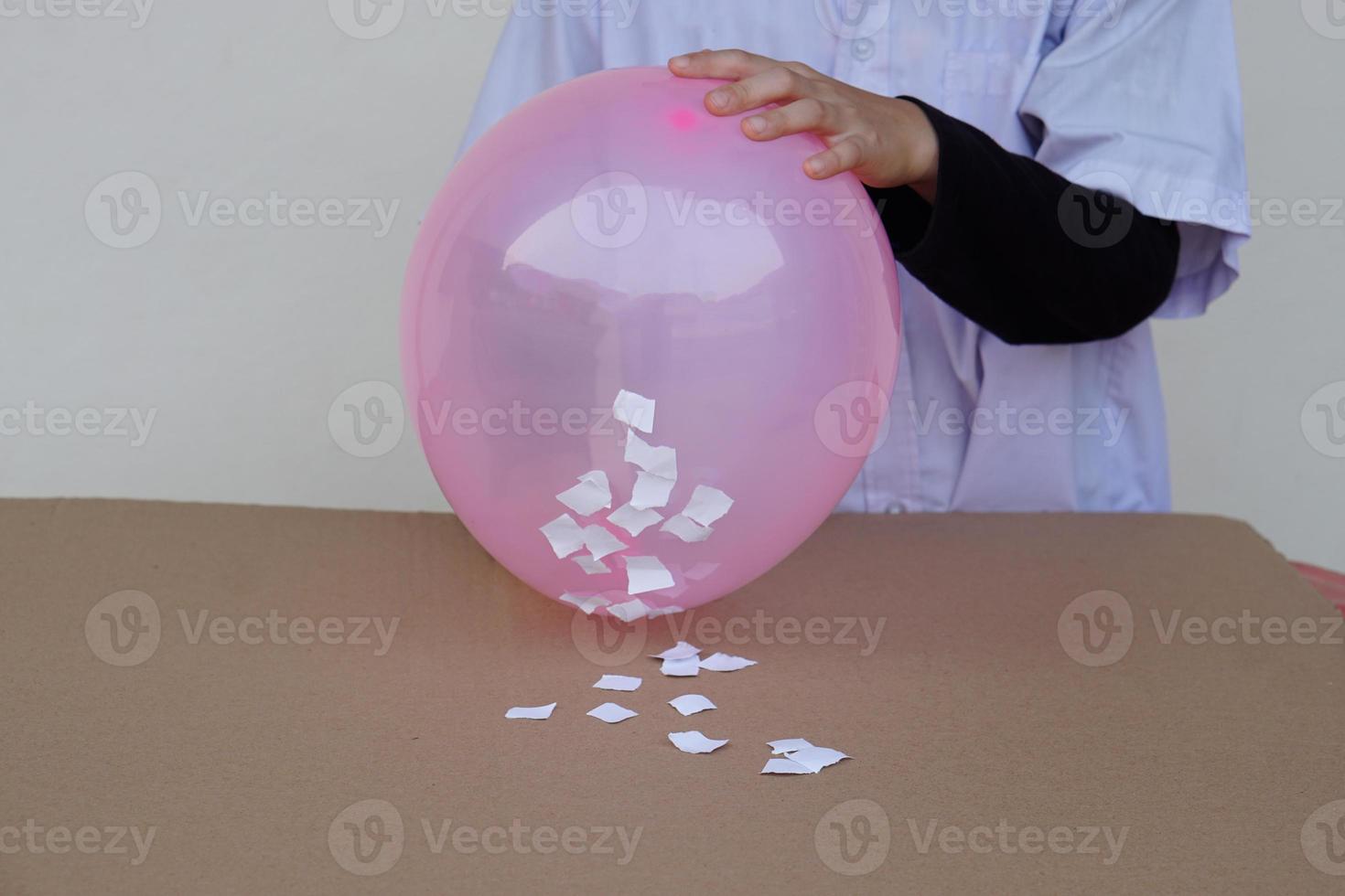 Closeup student do science experiment about static electricty from pink balloon and pieces of paper. Concept, Science project work activity. Learning by doing. Education. photo