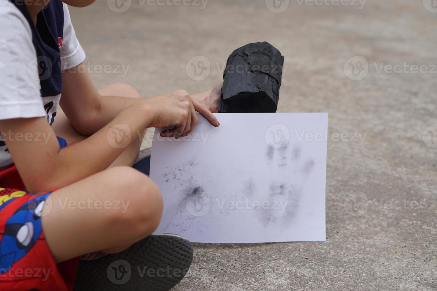 Close up boy holds white paper with stain of black charcoal, make hand print graffiti. Concept, learning by doing. Touch and observe  in science subject activity. Nature fuel photo