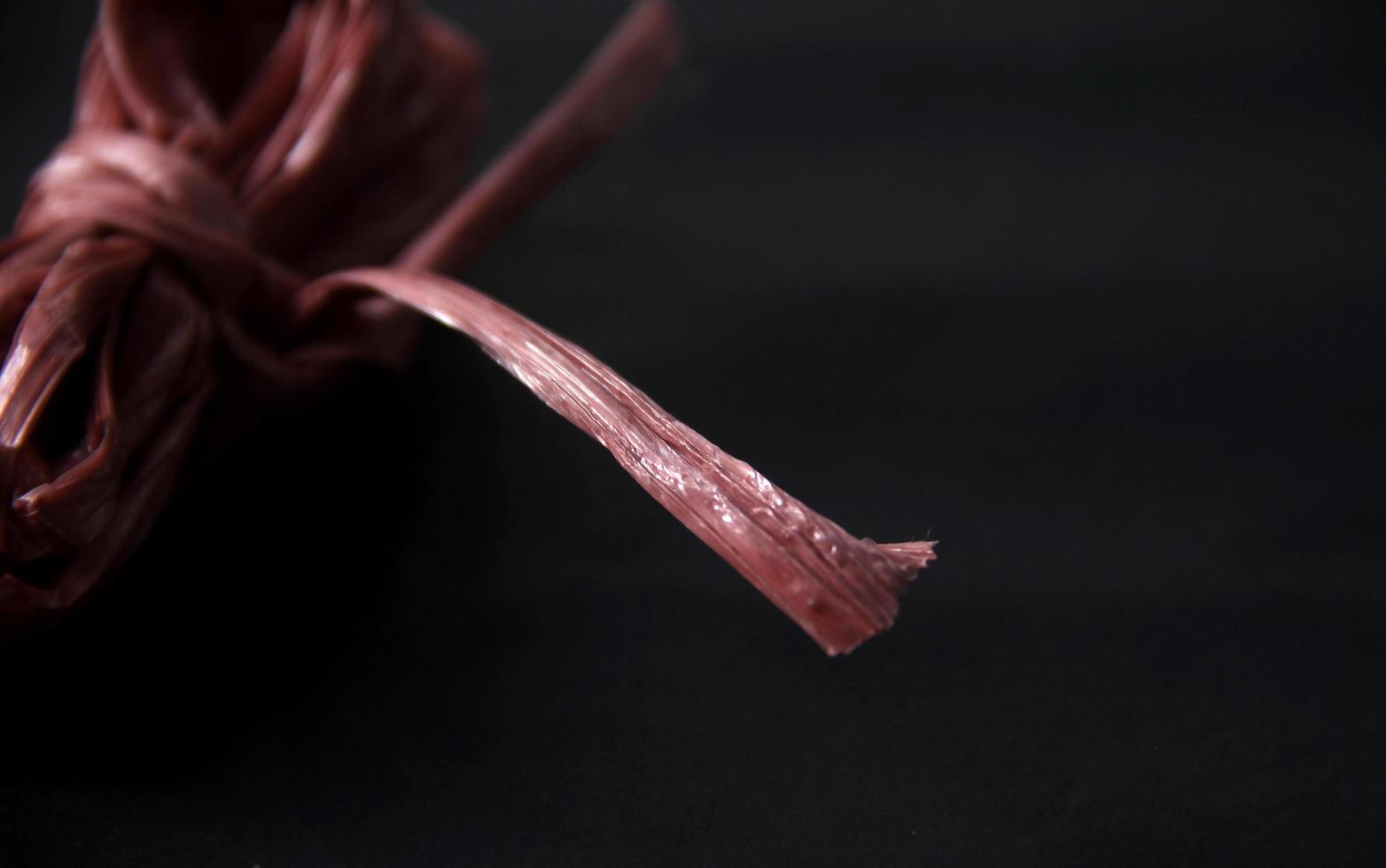 Close up red tali rafia. Raphia ribbon string strong heavy duty industrial equipment for wrapping cardboards or other big objects. Simple photo concept isolated on black background.