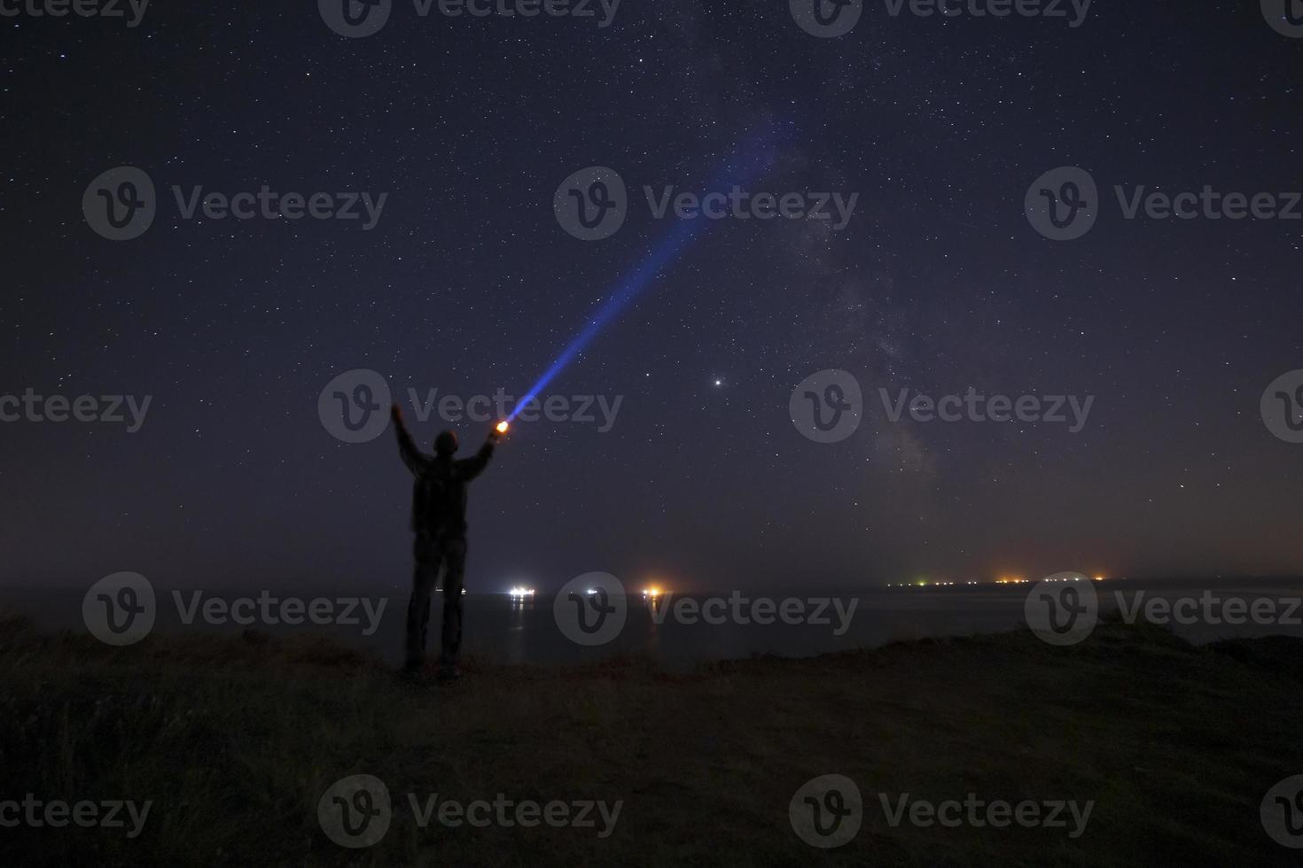 silhouette of man with flashlight beaming ray to Milky Way galaxy photo