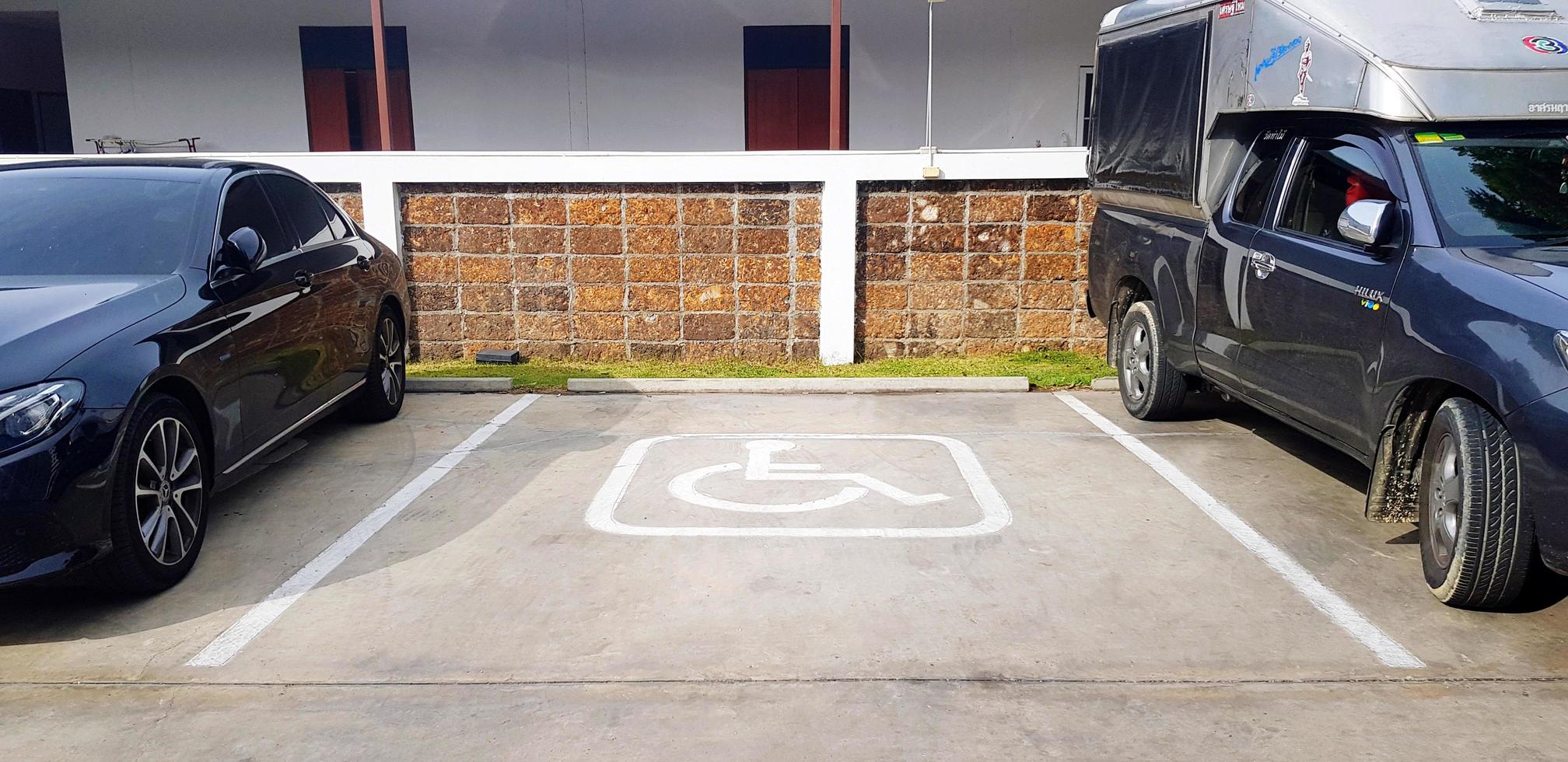 Songkhla, Thailand-March 9, 2023 The reservation parking of disabled people in middle or center between black car with brown brick wall background. Symbol, Restrict area and Reserve service concept photo