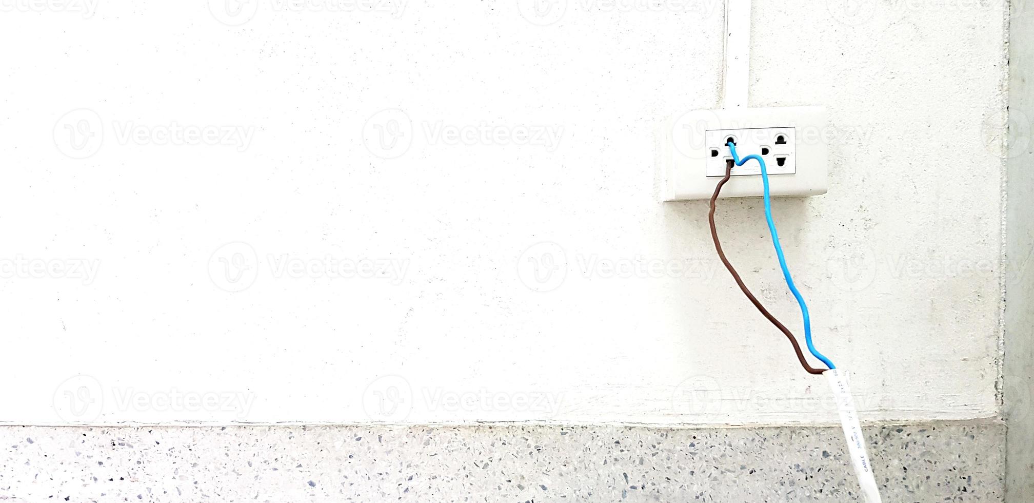 desnudo azul y marrón cable Instalar en pc y enchufe en a eléctrico toma de corriente caja en blanco cemento pared con tubería y Copiar espacio. inseguro instalación, seguridad, peligro y no estándar, corto circuito concepto foto