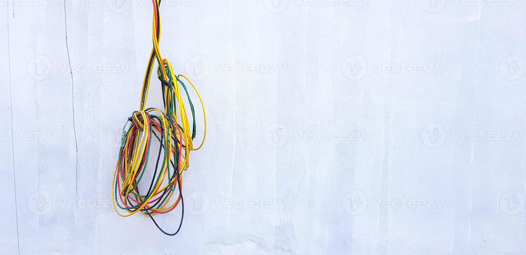 rojo, negro, amarillo y verde cable colgando o aislado en gris hormigón pared con Copiar espacio. nuevo instalación alambrado poder cable, conexión, reparar edificio y industrial eléctrico sistema foto