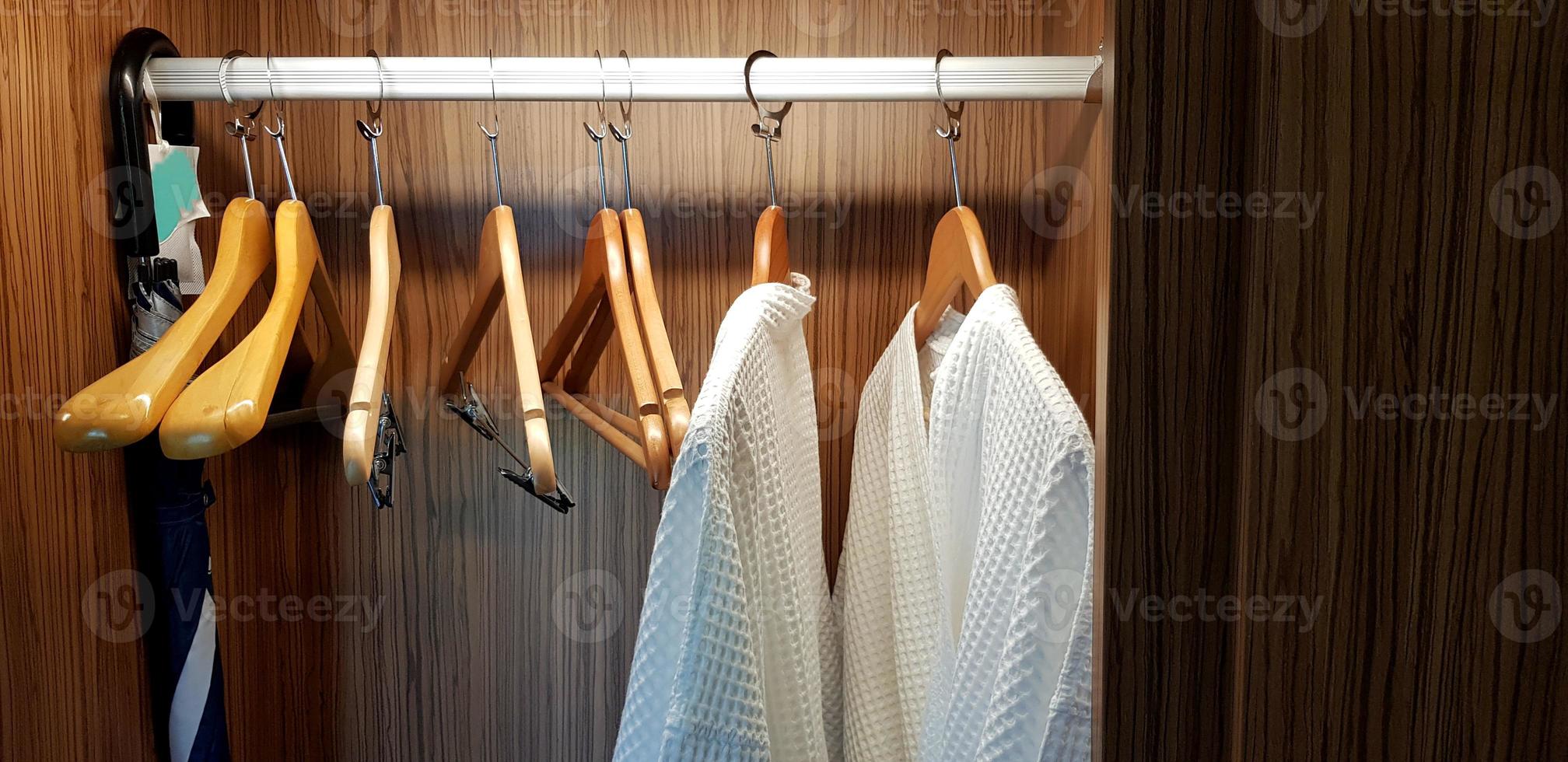 Two white clean bathrobes cloth or robe with wooden hanger and hanging inside dark brown closets with light for service customer wearing and taking shower at hotel photo