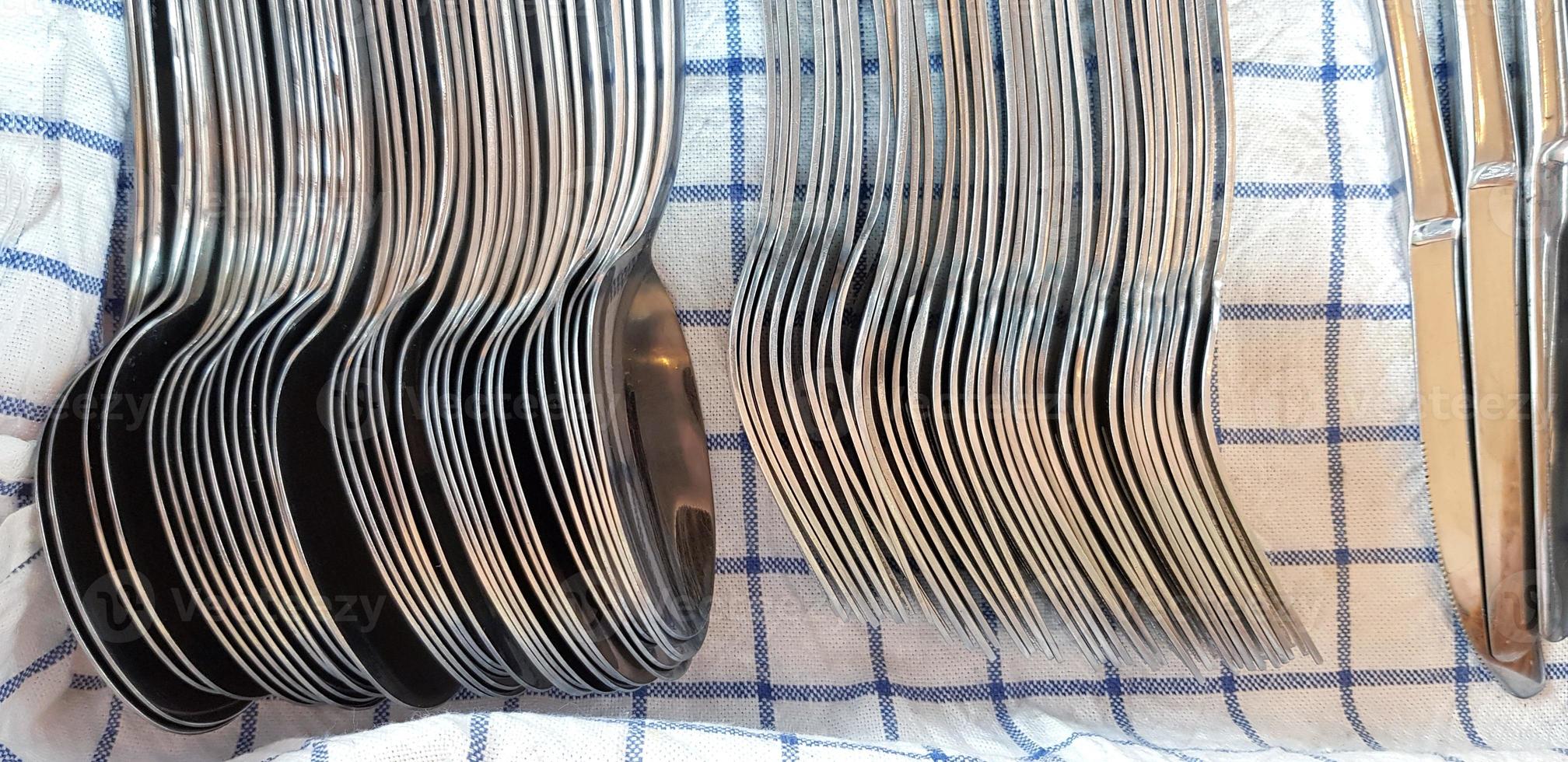 Stainless steel spoon, fork and knife putting and sorting tidy on blue and white plaid cotton for service customer use for eating food at restaurant. Group of object and Utensil concept photo