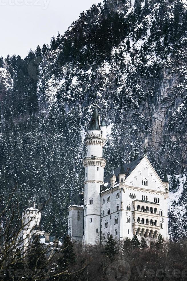 Beautiful view of the Neuschwanstein Castle or Schloss Neuschwanstein  on a winter day, with the mountains and trees capped with snow all around it. photo