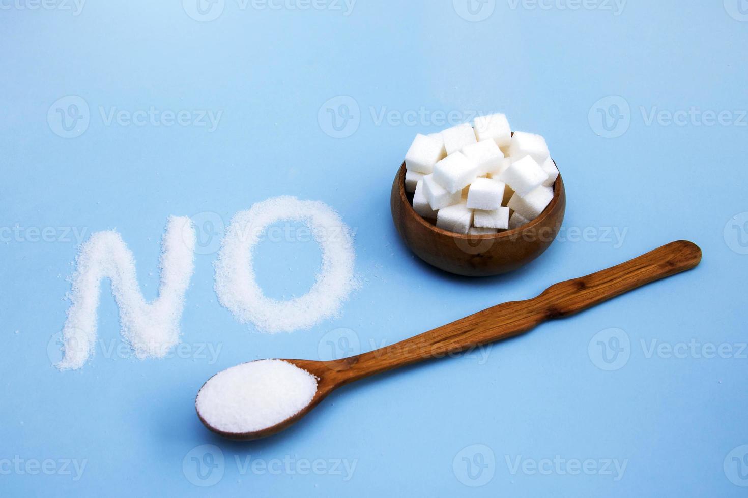 word no from sugar next to a wooden spoon with sugar and with a wooden bowl with lump sugar on a blue background, proper nutrition photo