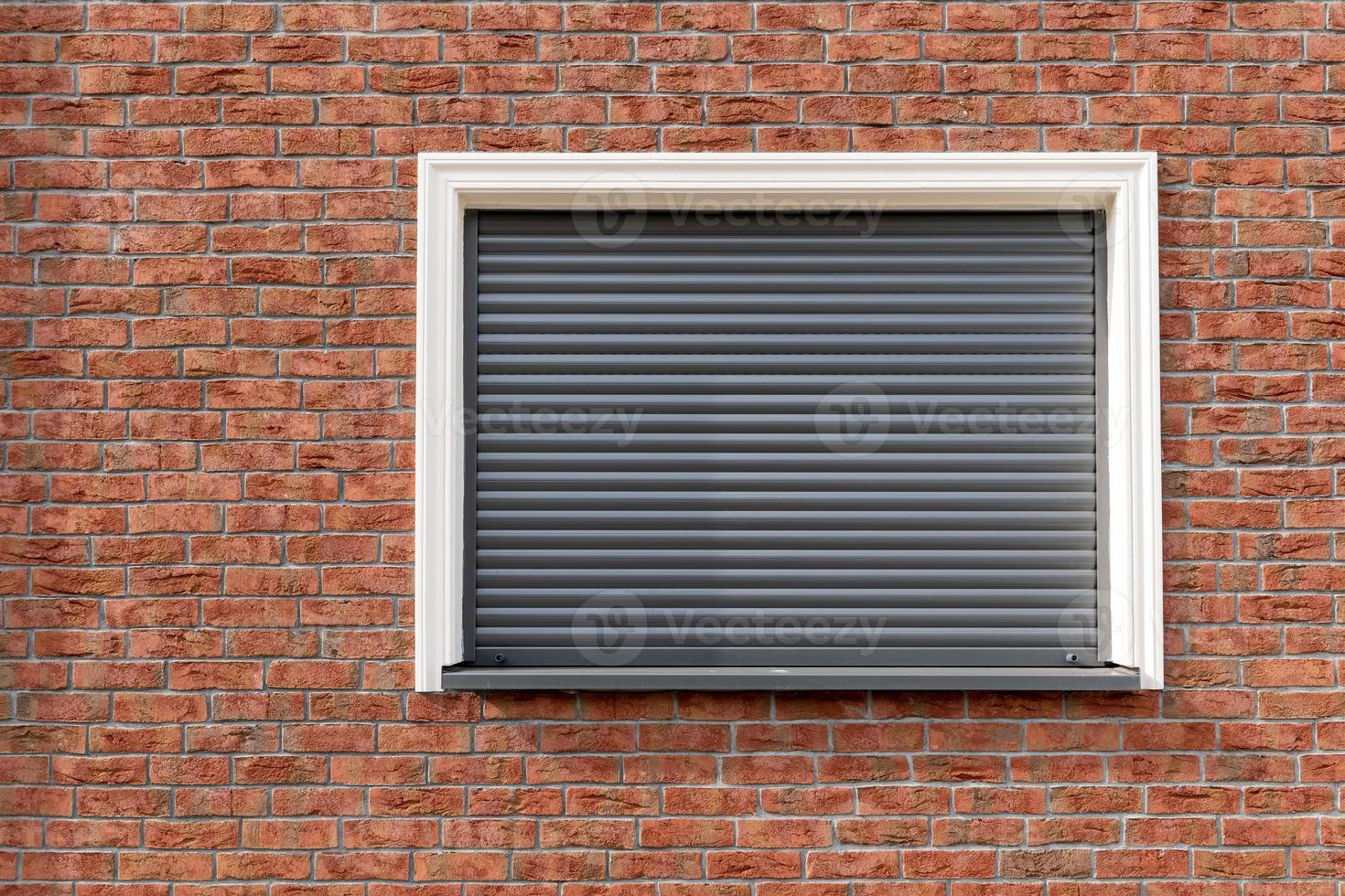 a brick wall with window and closed shutters photo