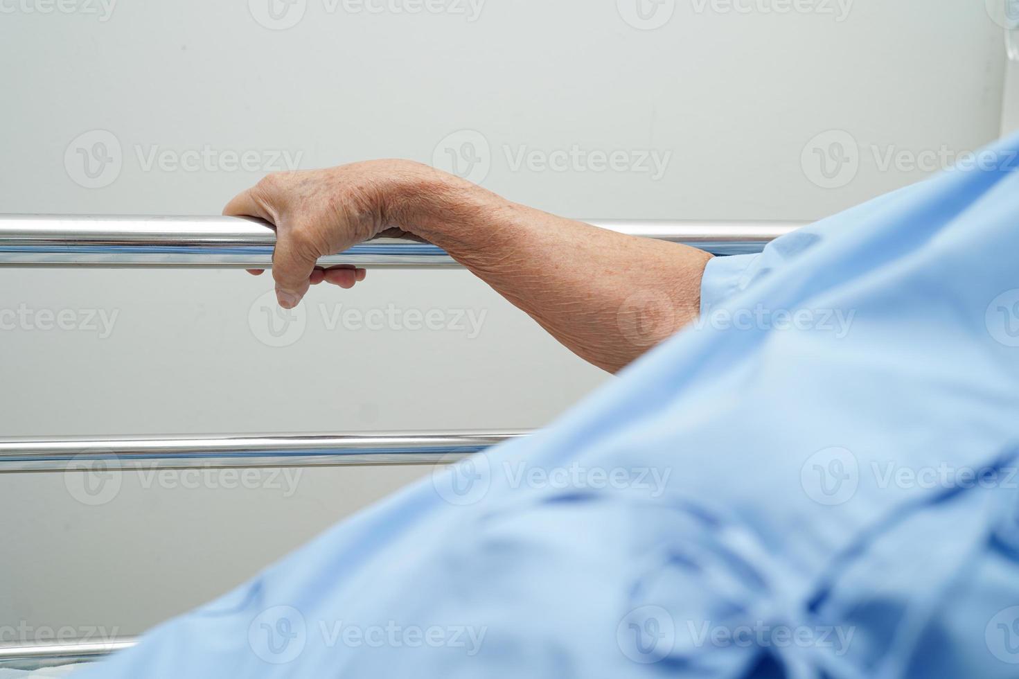 Asian elder senior woman patient holding bed rail while lie down with hope waiting her family in hospital. photo