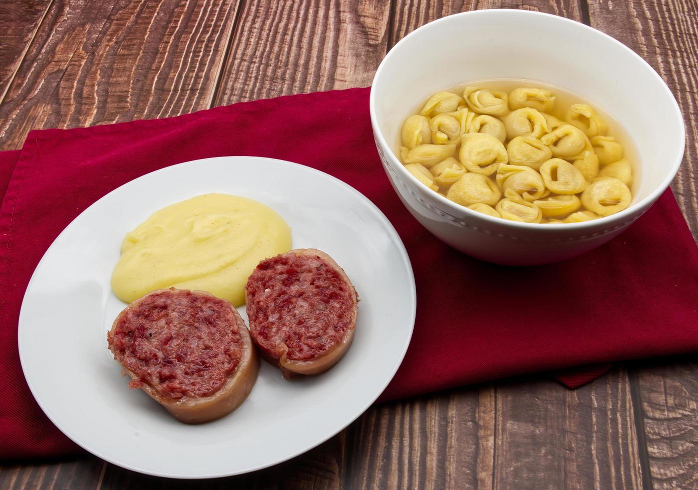 Slices of traditional Italian sausages Zampone di Modena with mashed potatoes and a Tortellini pasta dish. photo