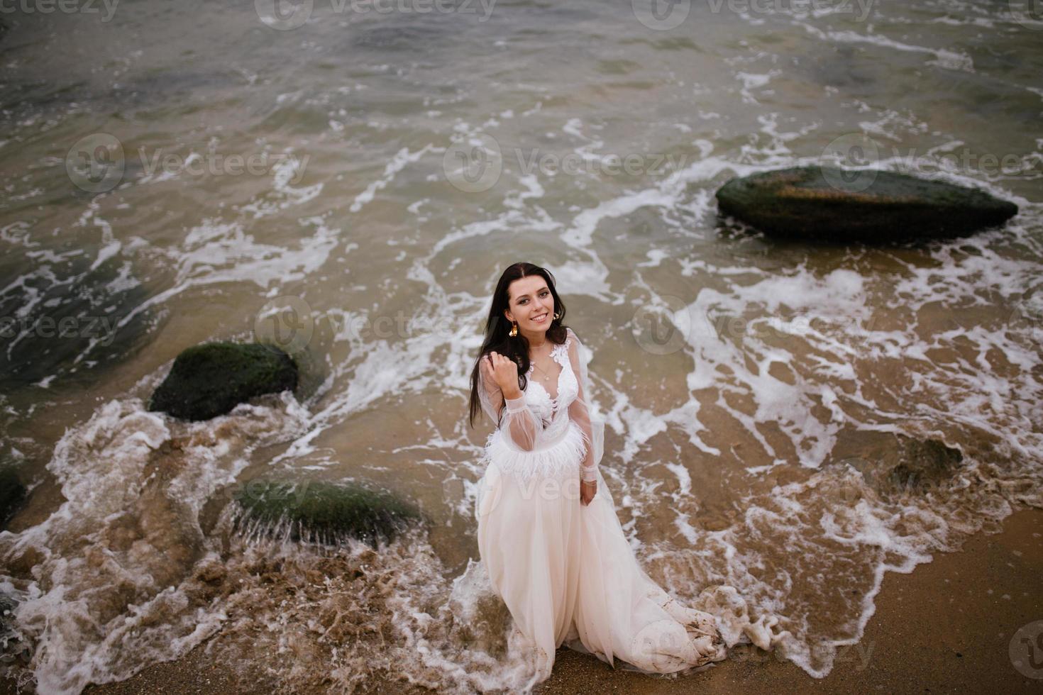Romantic beautiful bride in white dress posing on terrace with sea and mountains in background photo