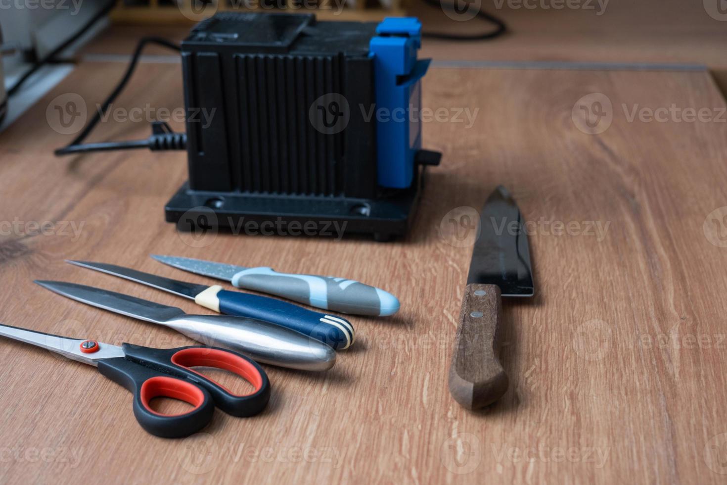 Sharpening a knife on an electric sharpener at home. Flatlay knife blade, scissors, sharpeners, dust flies on the machine. photo