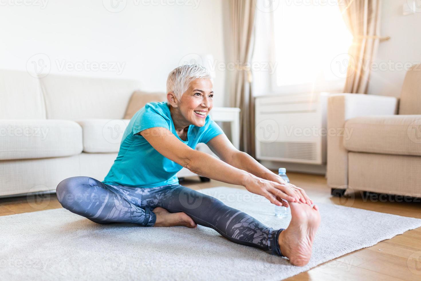 mayor mujer haciendo calentar rutina de ejercicio a hogar. aptitud mujer haciendo tramo ejercicio extensión su piernas, cuádriceps .anciano mujer vivo un activo estilo de vida. foto