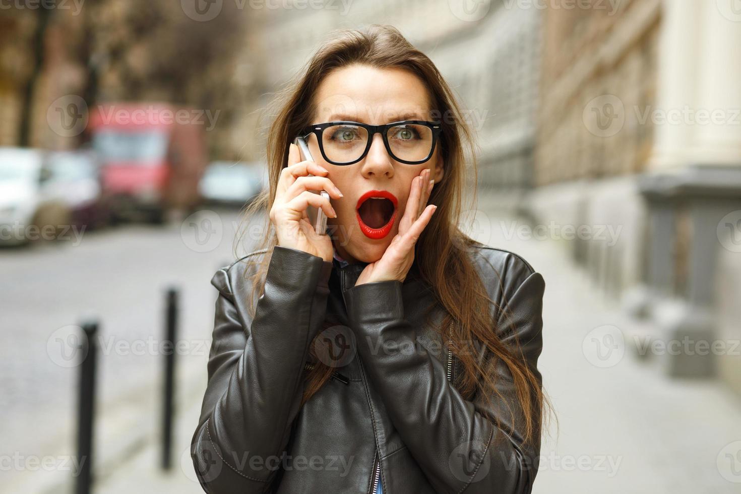 sorprendido mujer caminando abajo el calle mientras hablando en inteligente teléfono foto