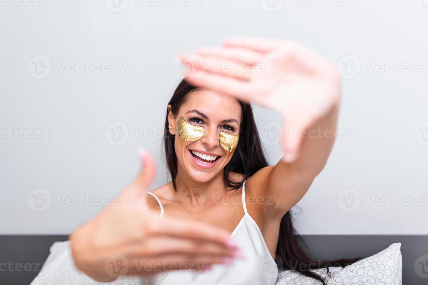 woman with Gold Cosmetics mask, Eye Patches.     Portrait of  Beautiful young woman with Gold Cosmetics mask, Eye Patches. sitting on bed and shows gesture photo frame with fingers. Portrai