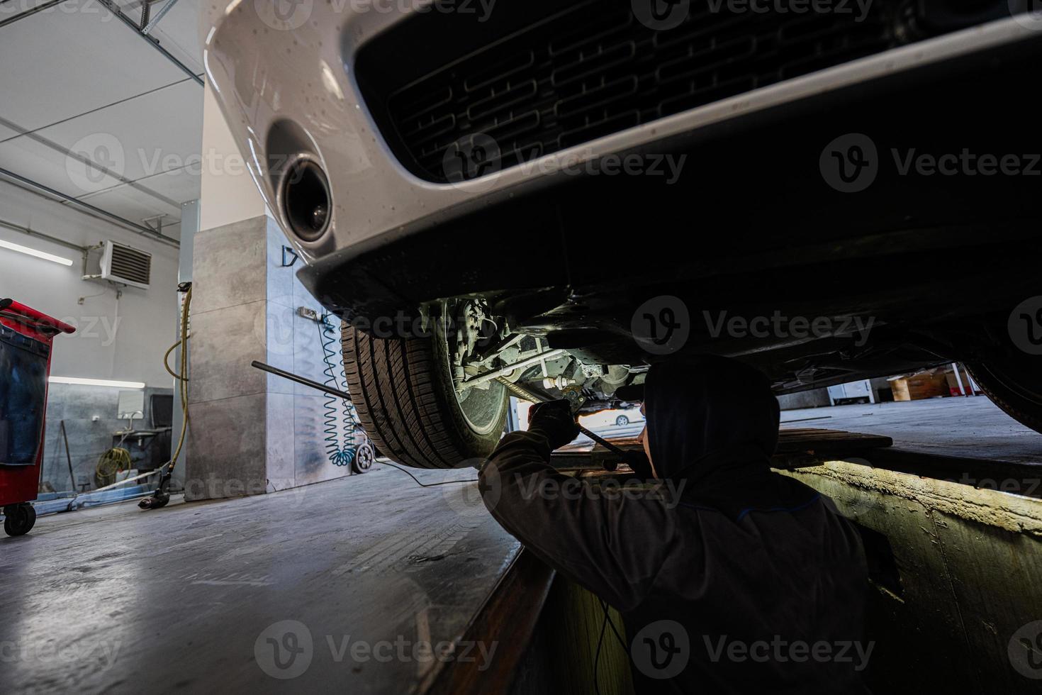 Mechanic in service repair station working with muscle car.  Inspects the running part of the wheel. photo
