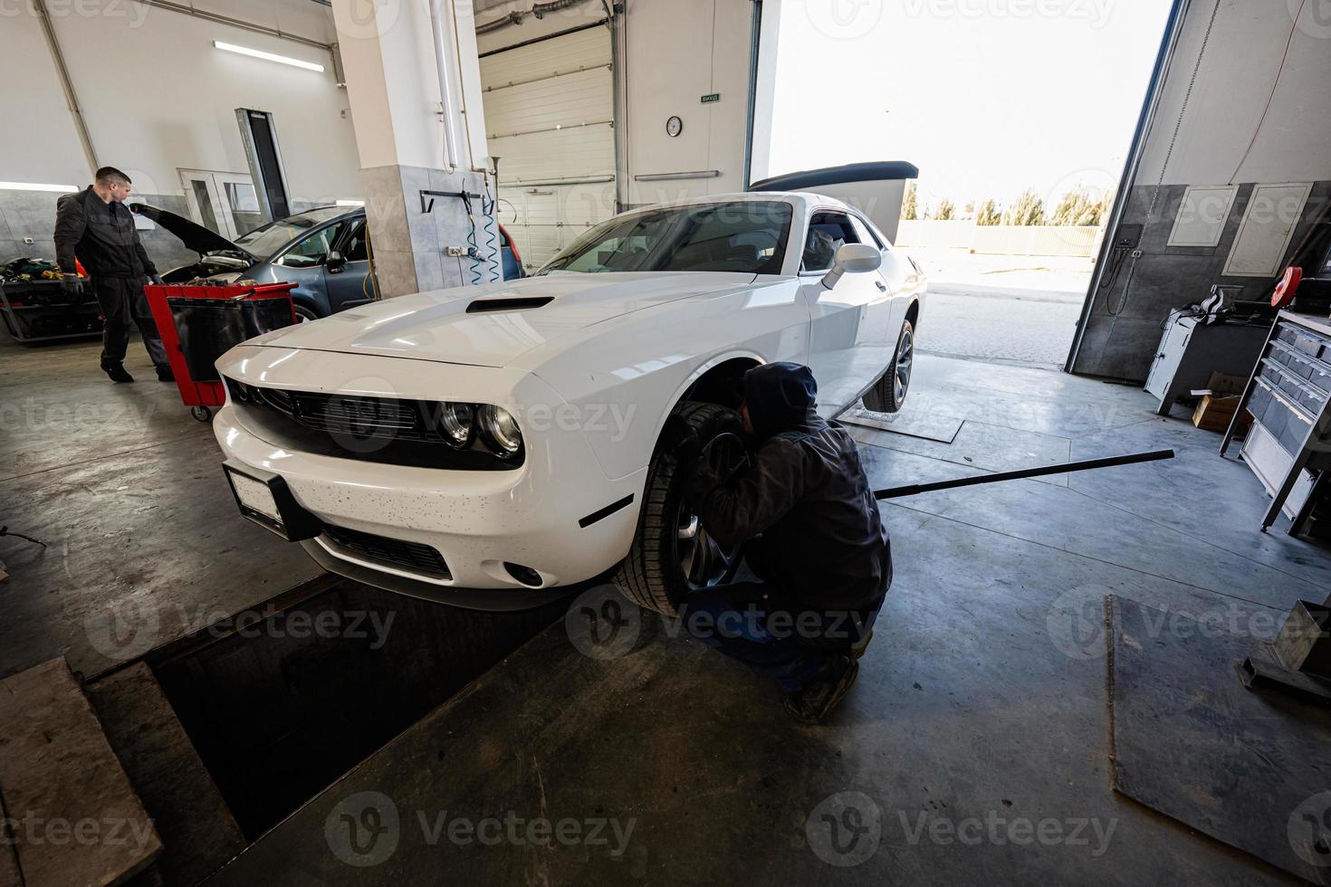 Mechanic in service repair station working with muscle car.  Man worker jacks up the car to diagnose the chassis. photo