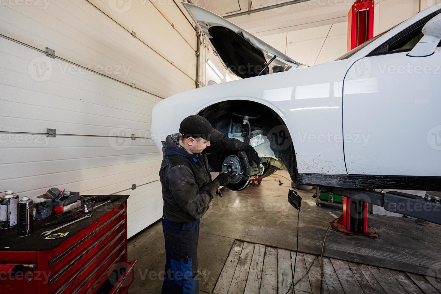 Mechanic in service repair station working with muscle car, dismantles a wheel on lift. photo