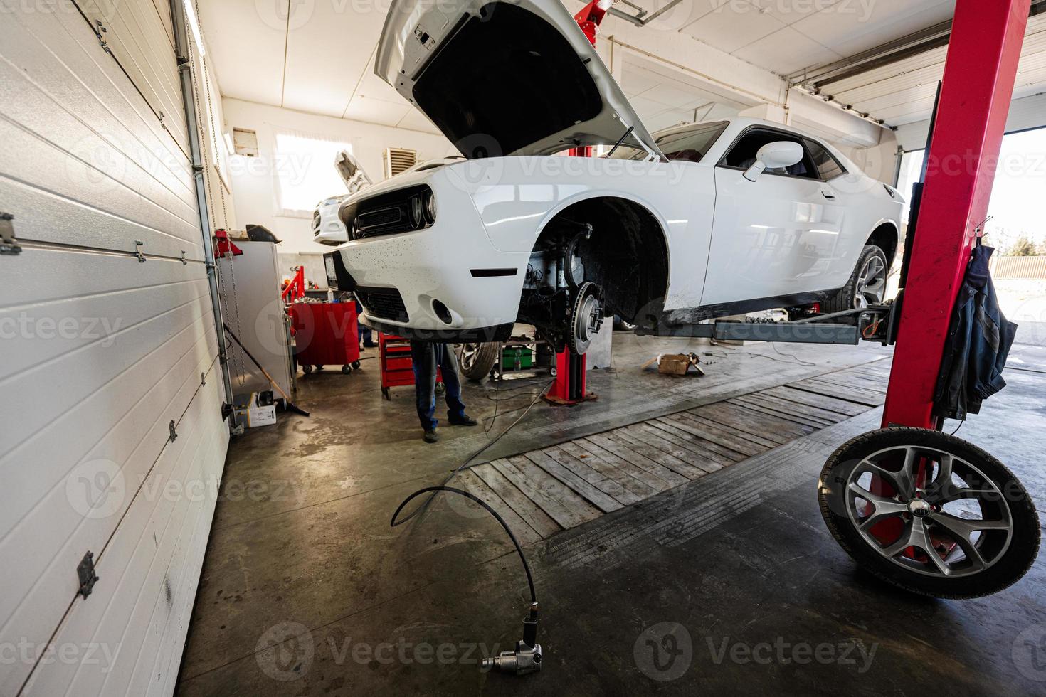 mecánico en la estación de reparación de servicio que trabaja con muscle car, desmantela una rueda en el ascensor. foto