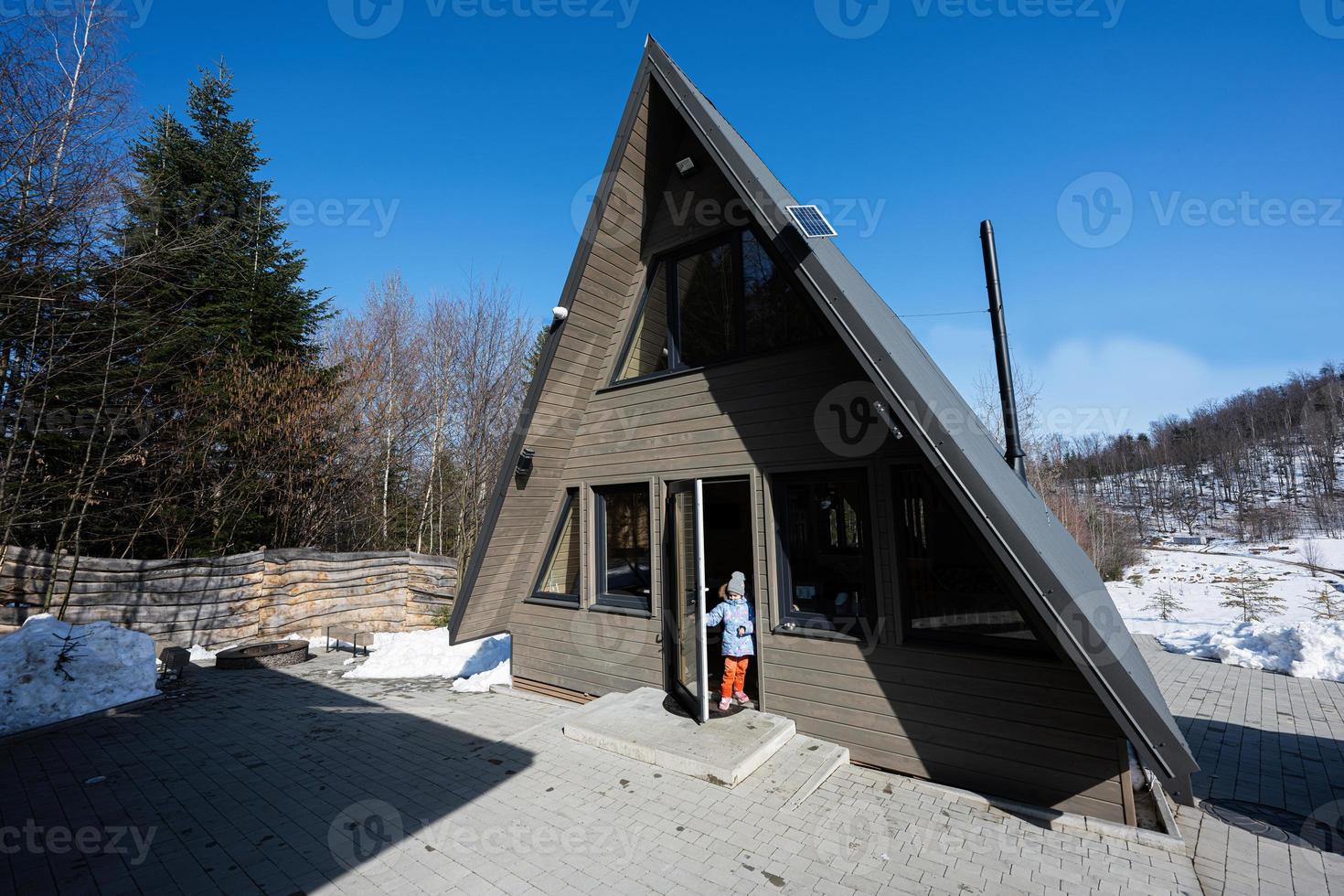 pequeño niña estar en puerta de triángulo país minúsculo cabina casa en montañas. foto