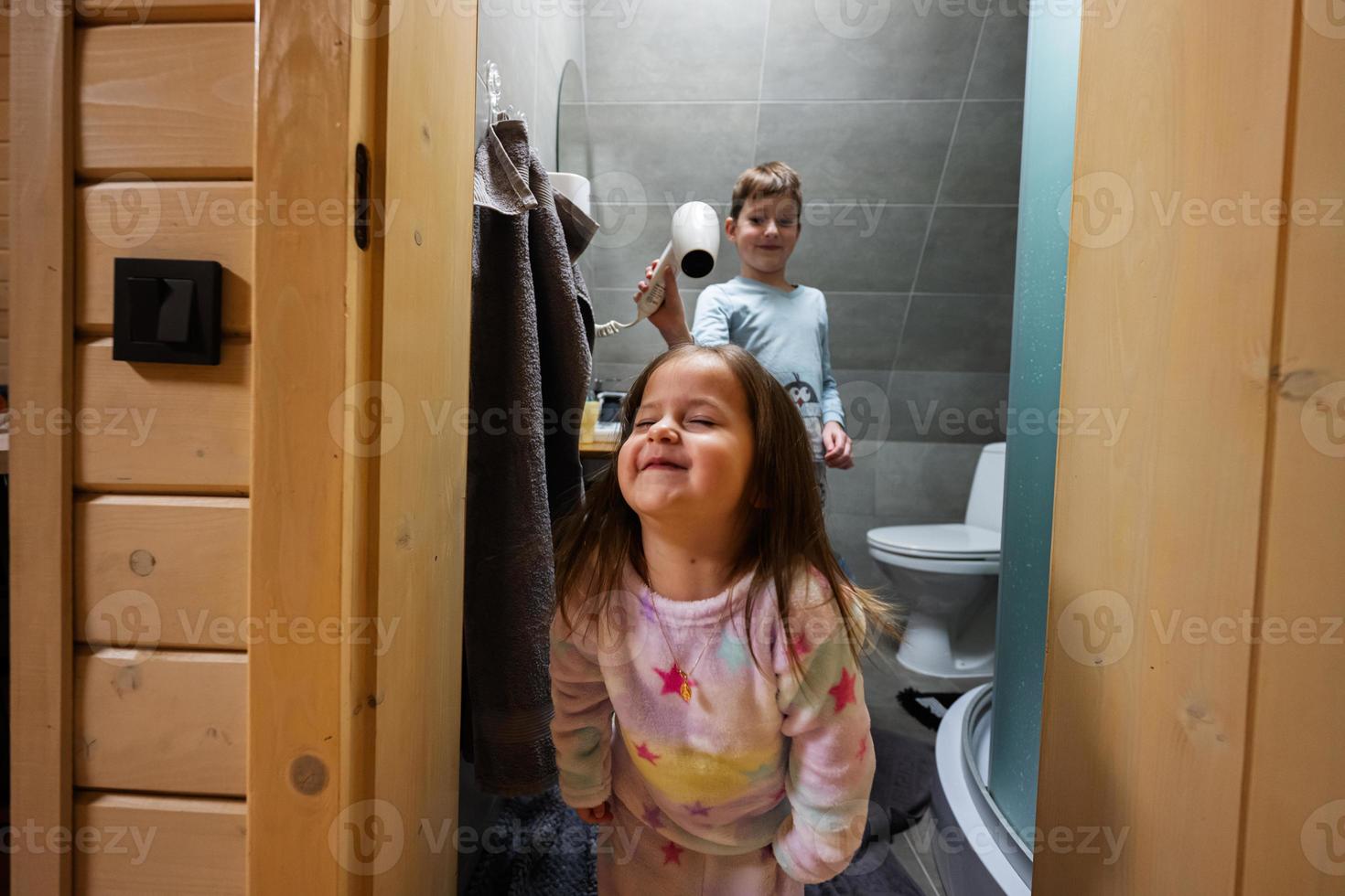 Brother dries sister hair with a hair dryer at bathroom. photo