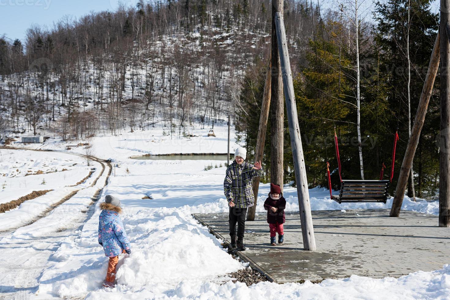 Older brother with younger sisters play near big wooden swing in forest of mountains. photo