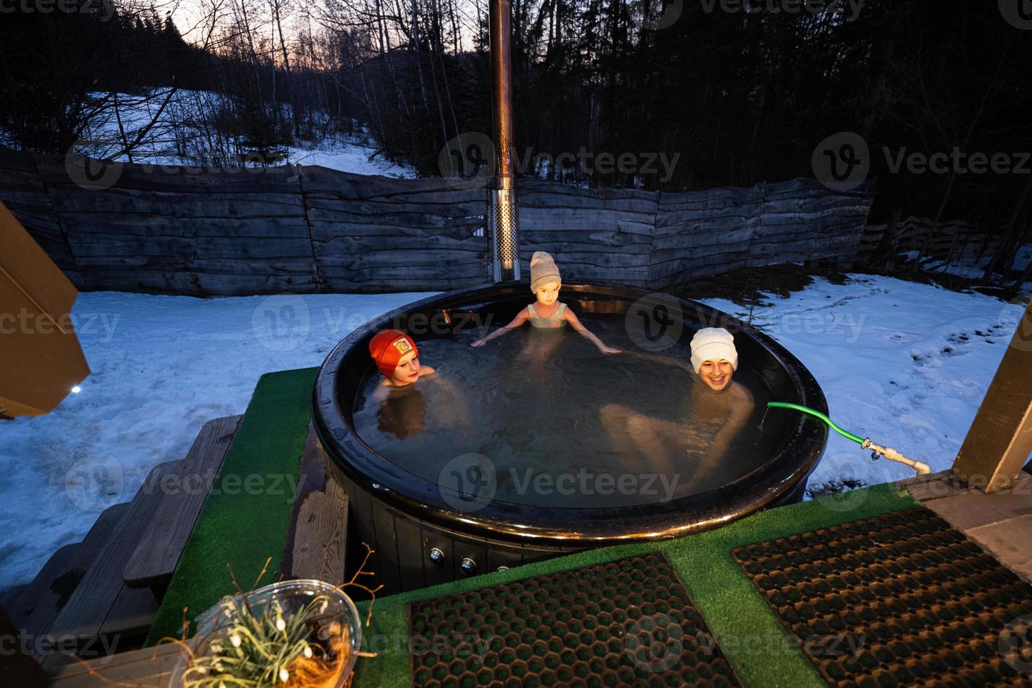 Kids enjoying bathing in wooden barrel hot tub in the terrace of the cottage. Scandinavian bathtub with a fireplace to burn wood and heat water. photo