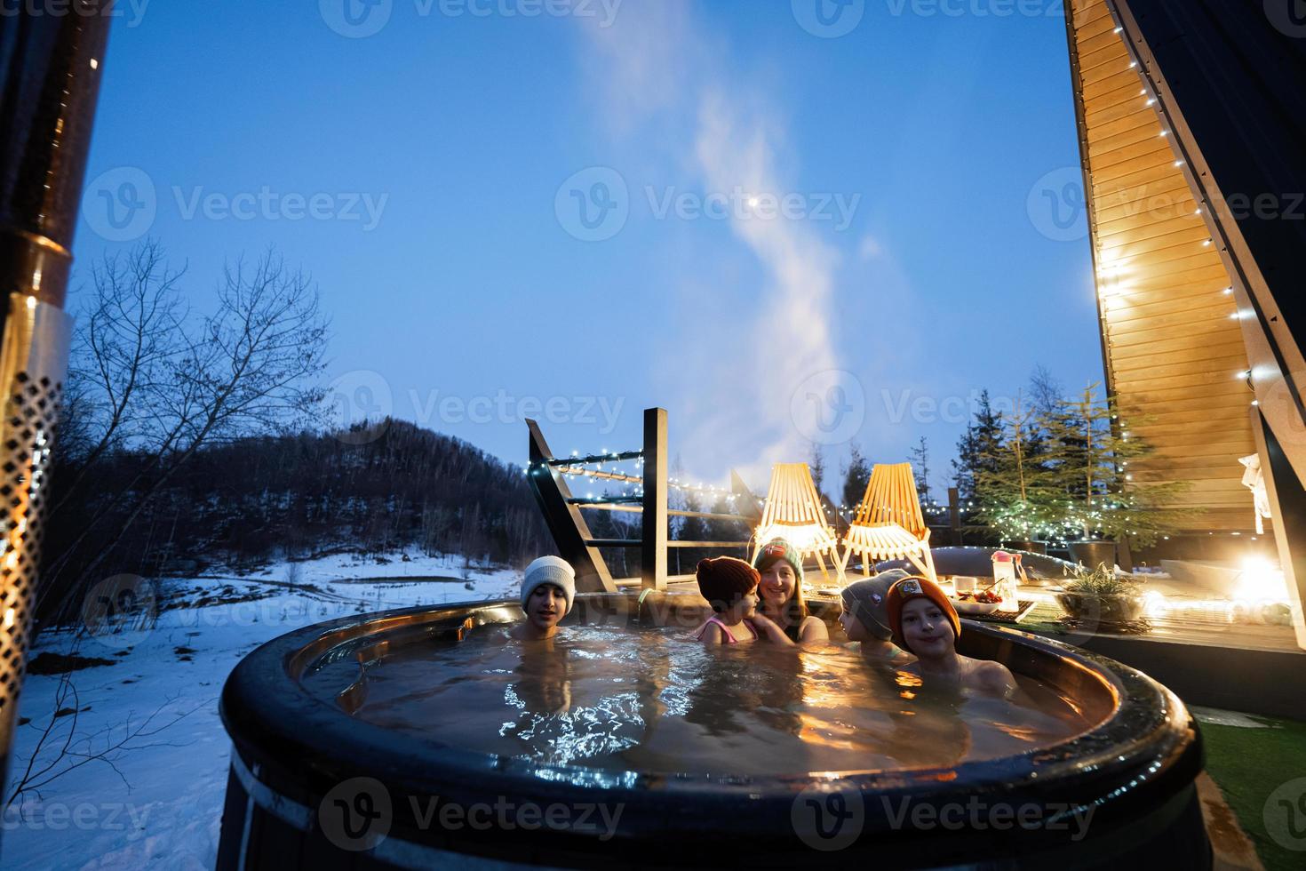 Family enjoying bathing in wooden barrel hot tub in the terrace of the cottage. Scandinavian bathtub with a fireplace to burn wood and heat water. photo