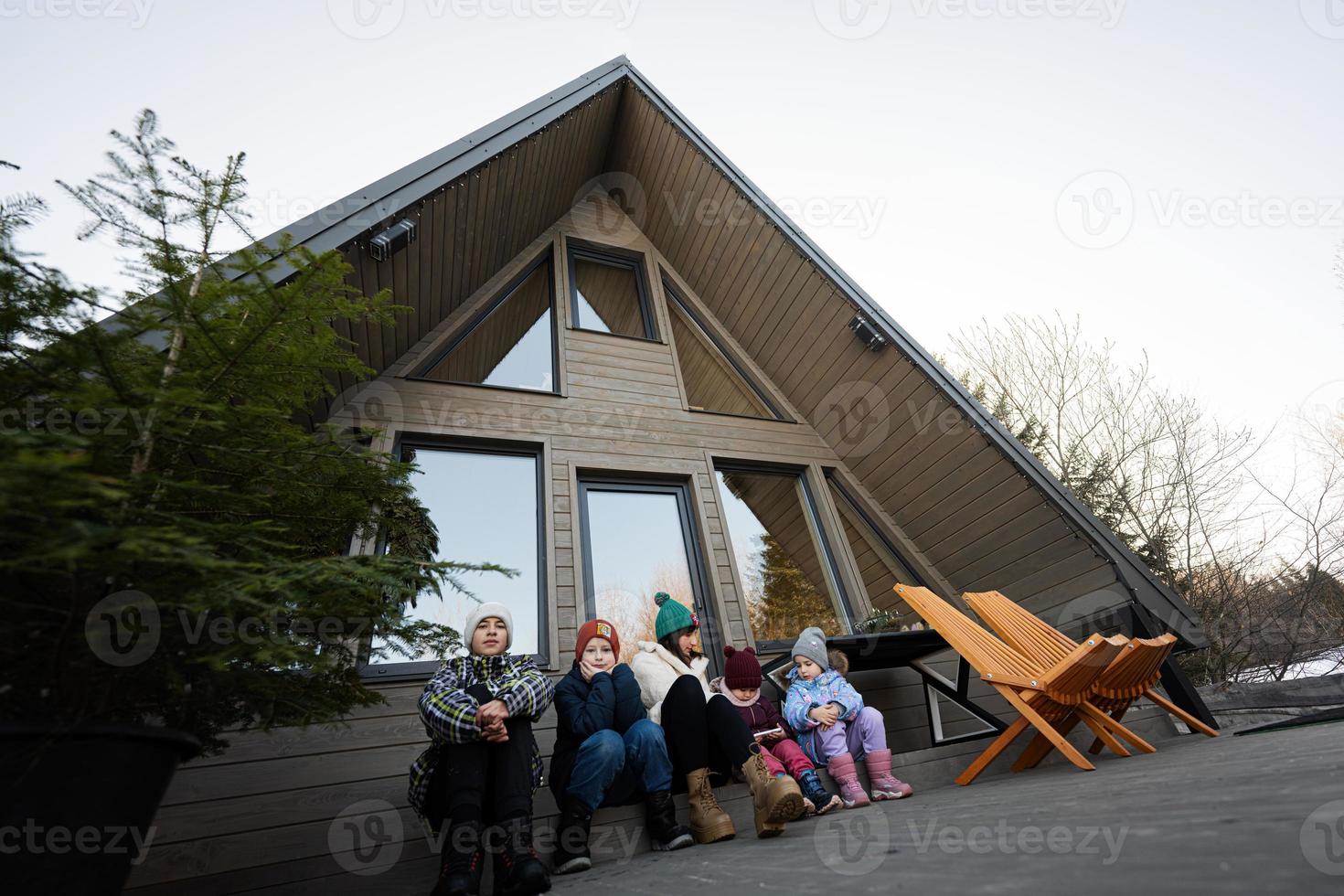madre con cuatro niños sentar en terraza apagado cuadrícula minúsculo casa en el montañas. foto
