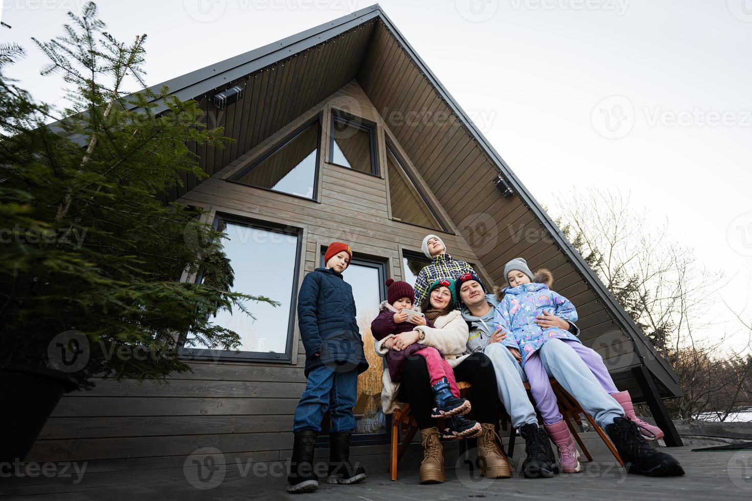 grande familia con cuatro niños sentar en terraza apagado cuadrícula minúsculo casa en el montañas. foto