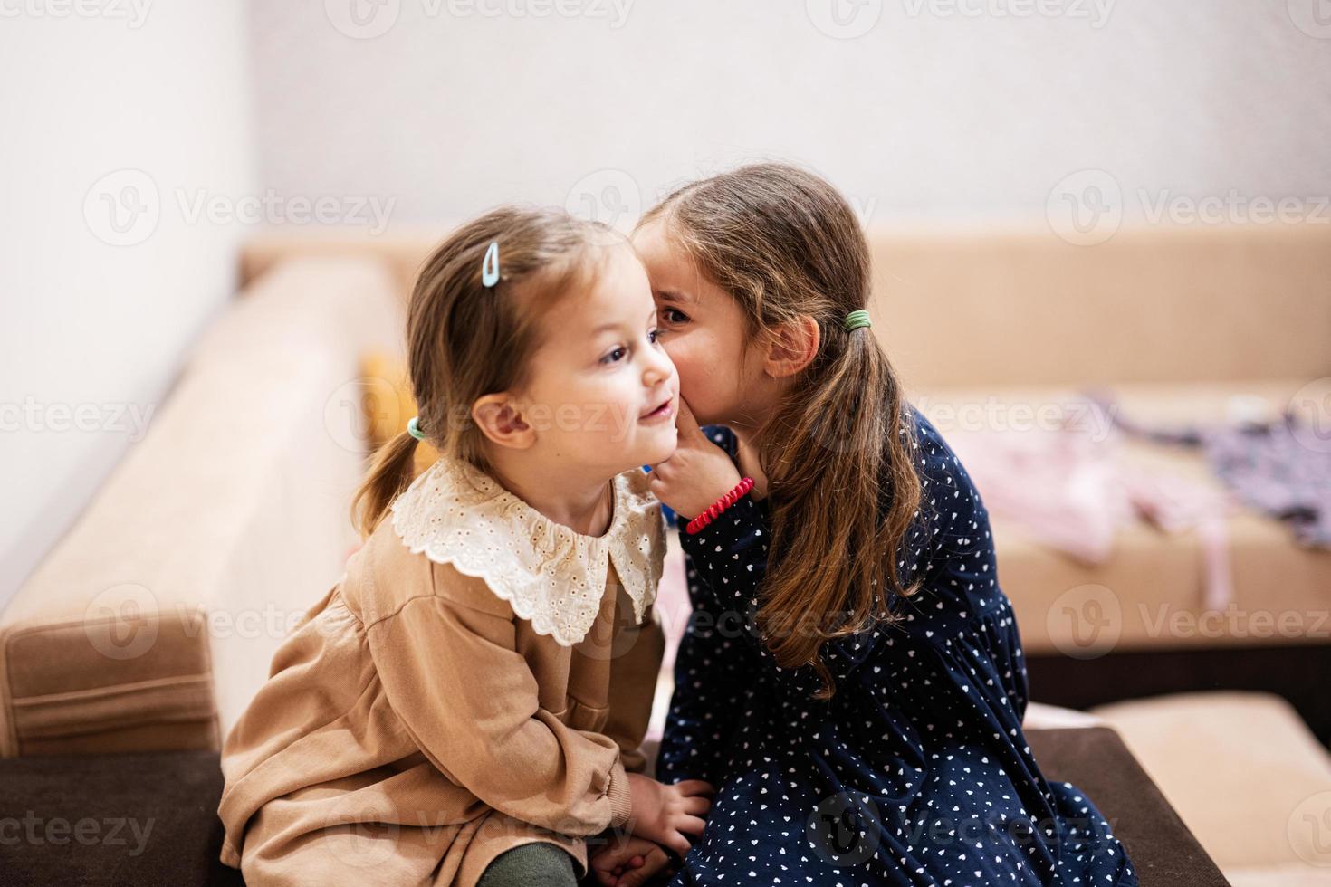 Two sisters sit on the sofa and tell and share girlish secrets with each other. photo