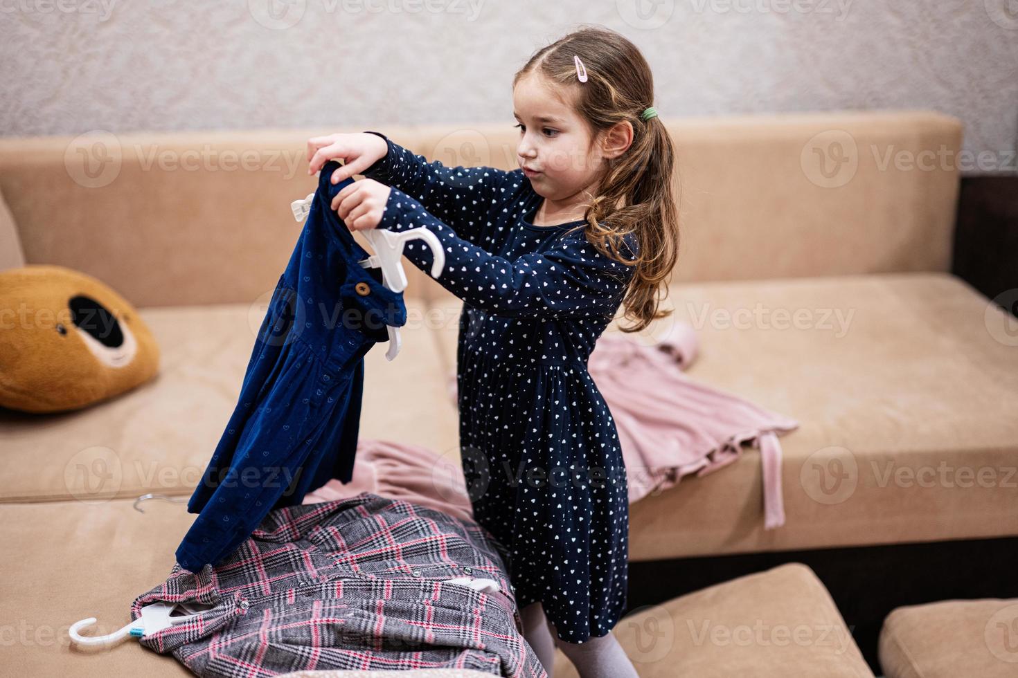 bebé niña elegir ropa desde el guardarropa a hogar en el sofá. foto