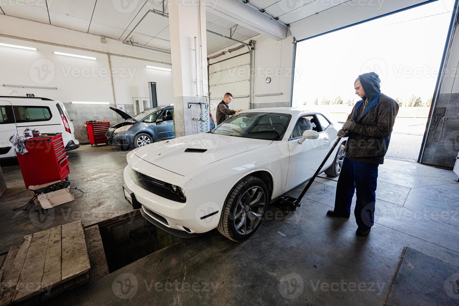 Two service man mechanics in repair station working with muscle car.  Man worker jacks up the car to diagnose the chassis. photo
