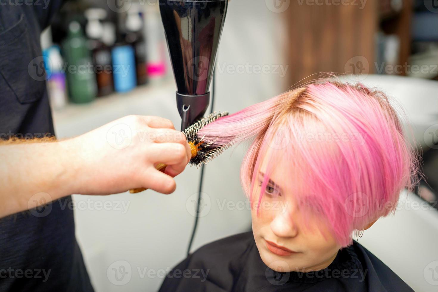 Hairdresser dries pink hair of woman photo