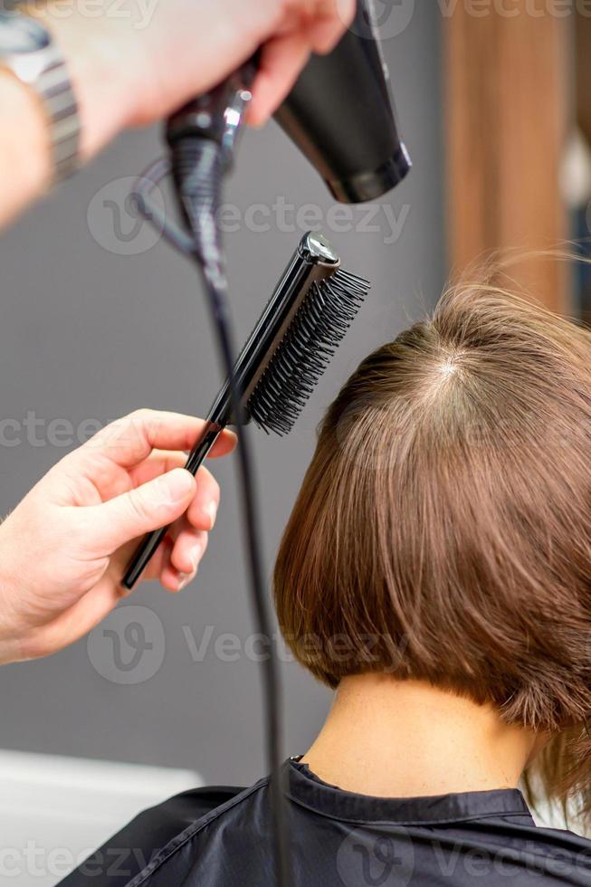 Hairdresser dries brown hair of woman photo