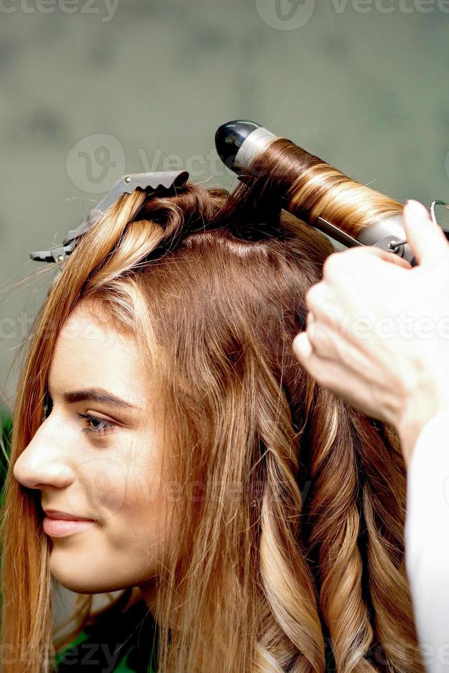 Hairdresser makes curls with curling iron photo