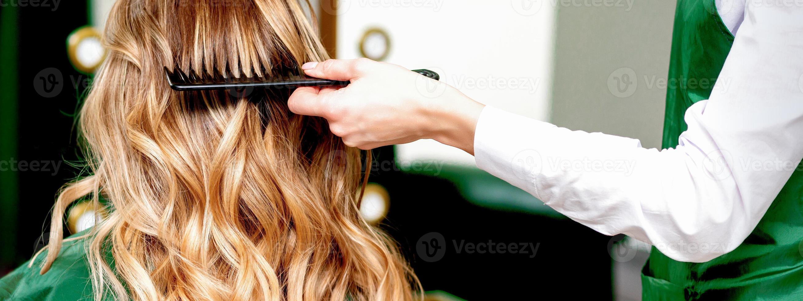 Hairdresser combing wavy hair of woman photo