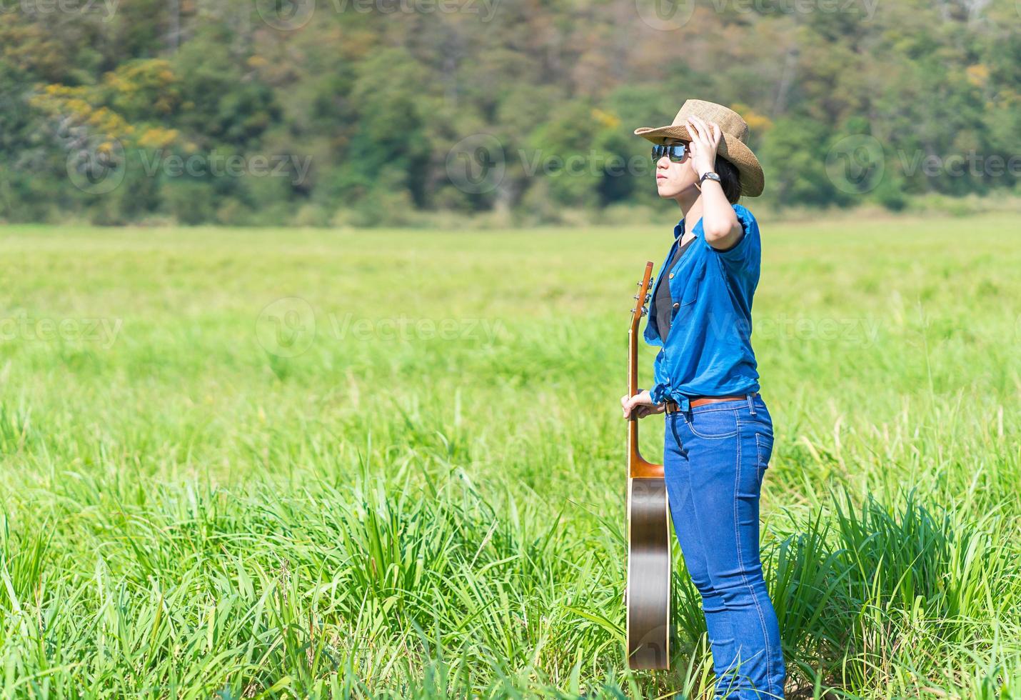 Woman wear hat and carry her guitar in grass field photo