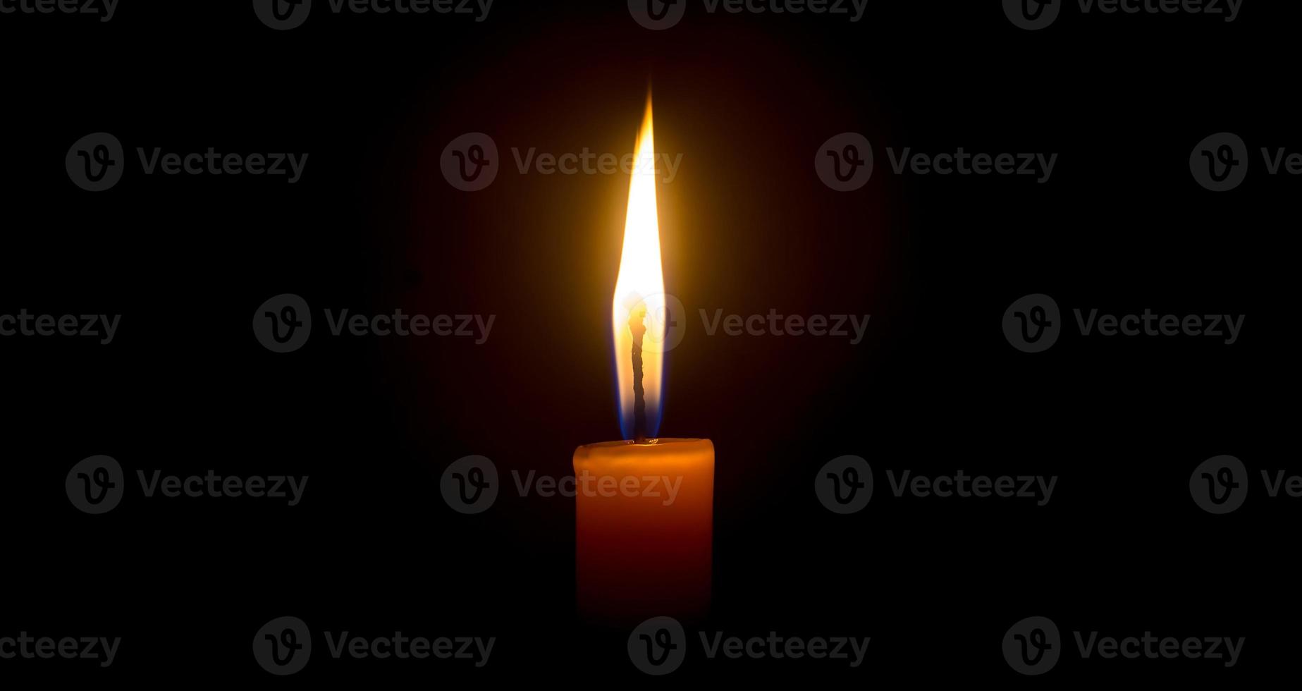 A single burning candle flame or light glowing on an orange candle on black or dark background on table in church for Christmas, funeral or memorial service with copy space photo