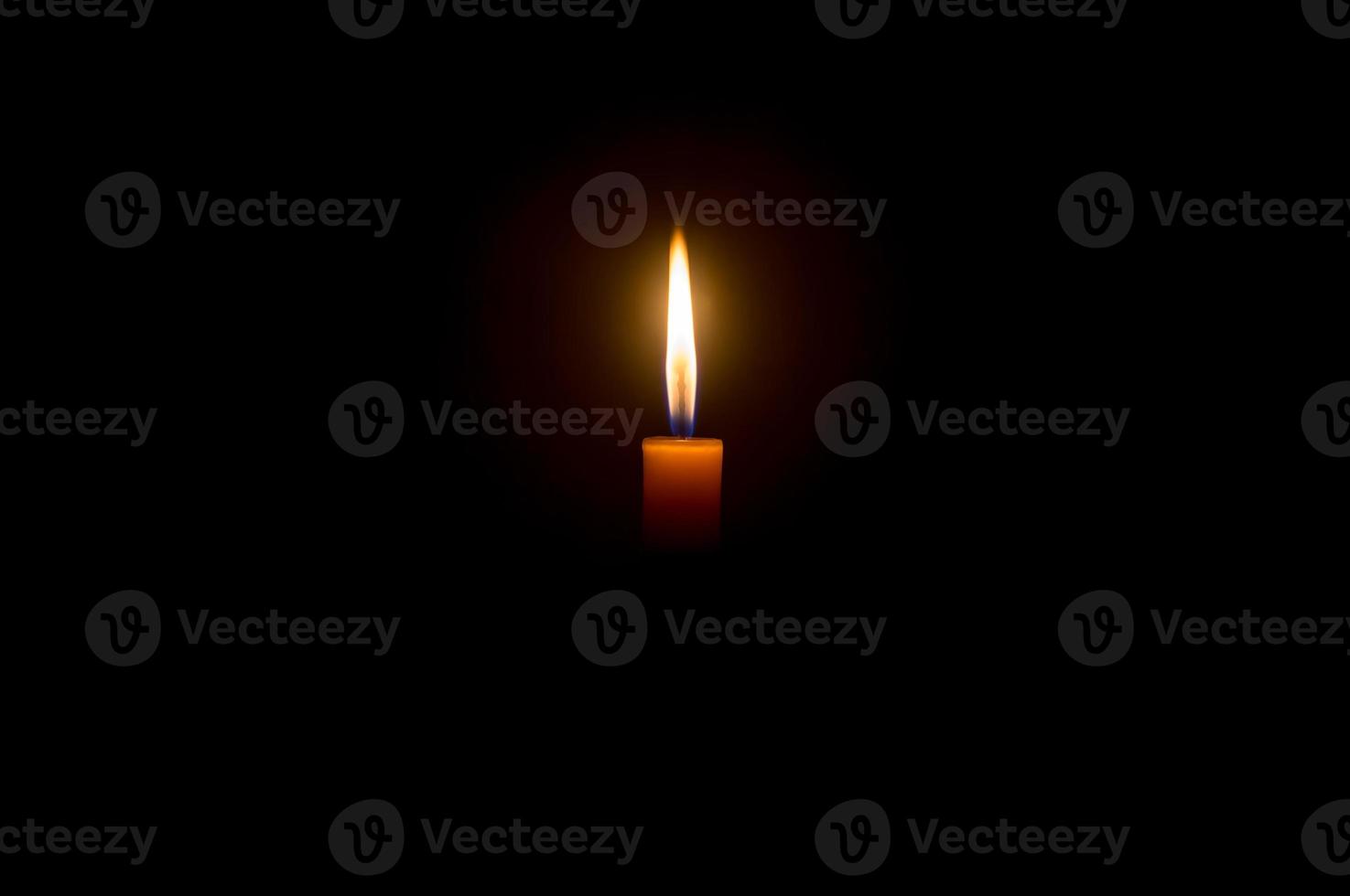 A single burning candle flame or light glowing on an orange candle on black or dark background on table in church for Christmas, funeral or memorial service with copy space photo