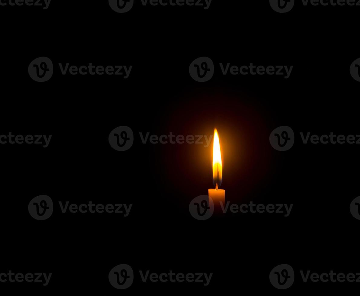 A single burning candle flame or light glowing on an orange candle on black or dark background on table in church for Christmas, funeral or memorial service with copy space photo