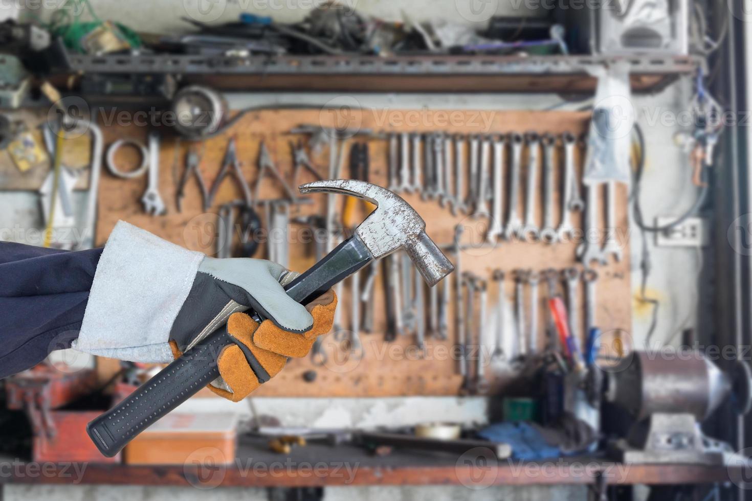 Hand in glove holding hammer with tools hanging photo