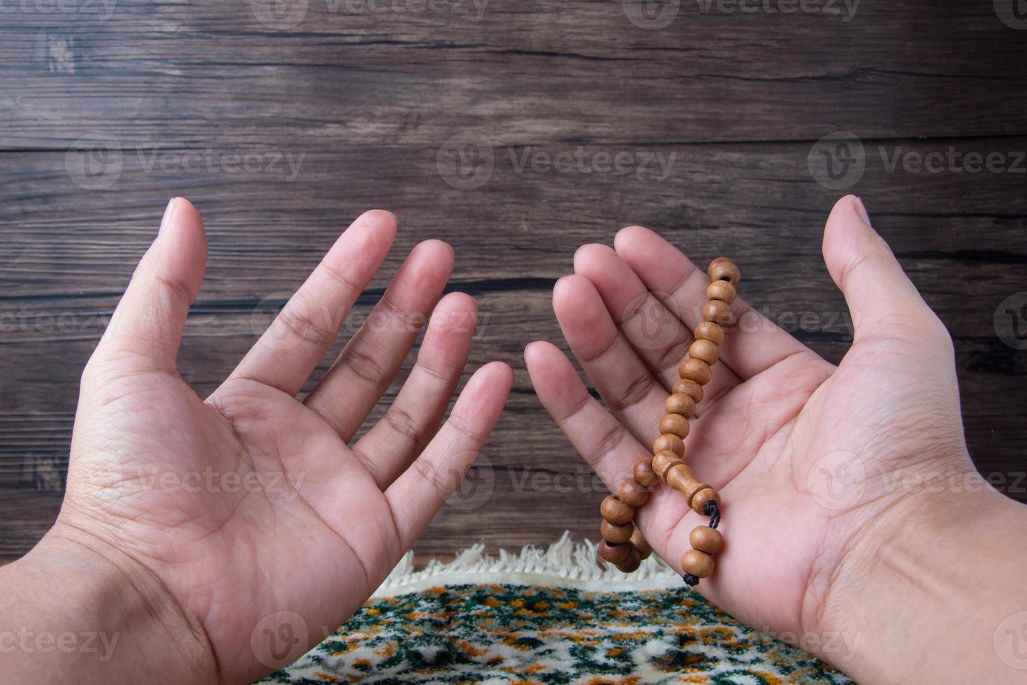 Muslim man hands praying and carrying prayer beads, on a prayer rug on a wooden background and in the sun, empty space, copy space, photo