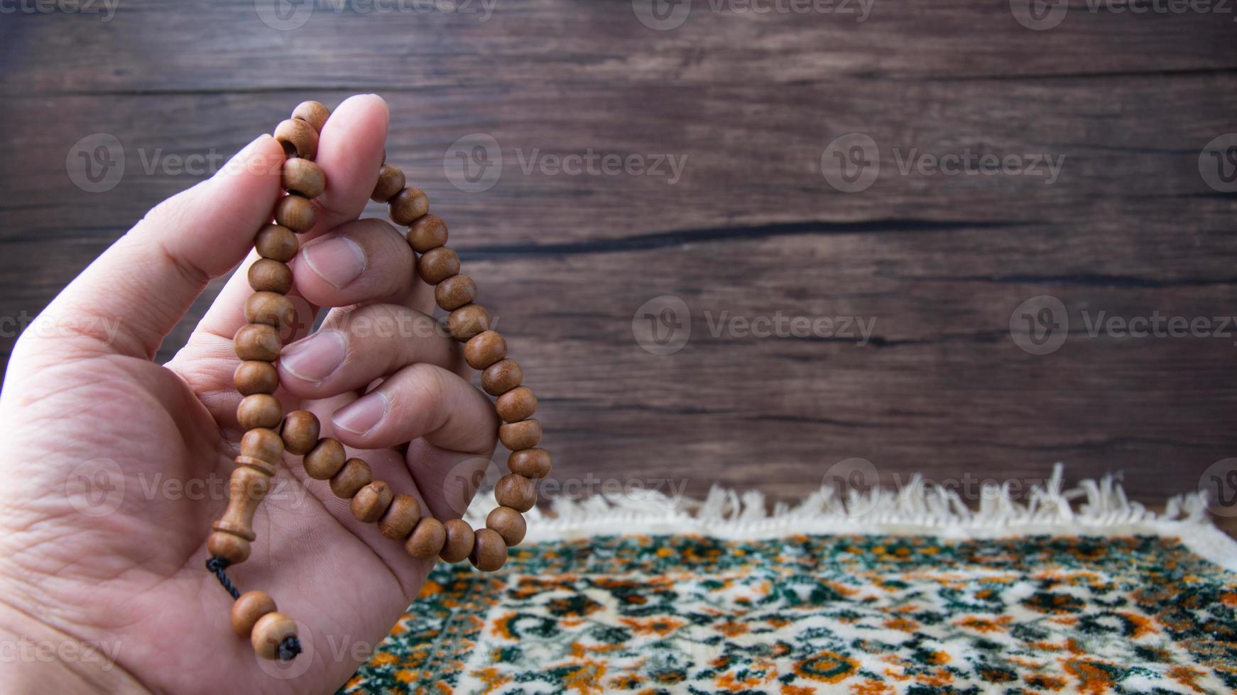 praying, palms up when praying in Islamic culture, carrying prayer beads on a prayer rug on a wooden background and there is sunshine, empty space, copy space, photo